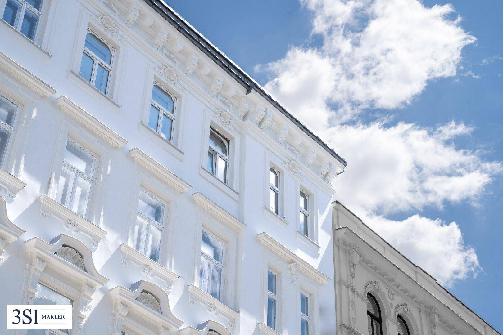 Nahaufnahme einer strahlend weißen Fassade mit klassischen Verzierungen unter blauem Himmel.