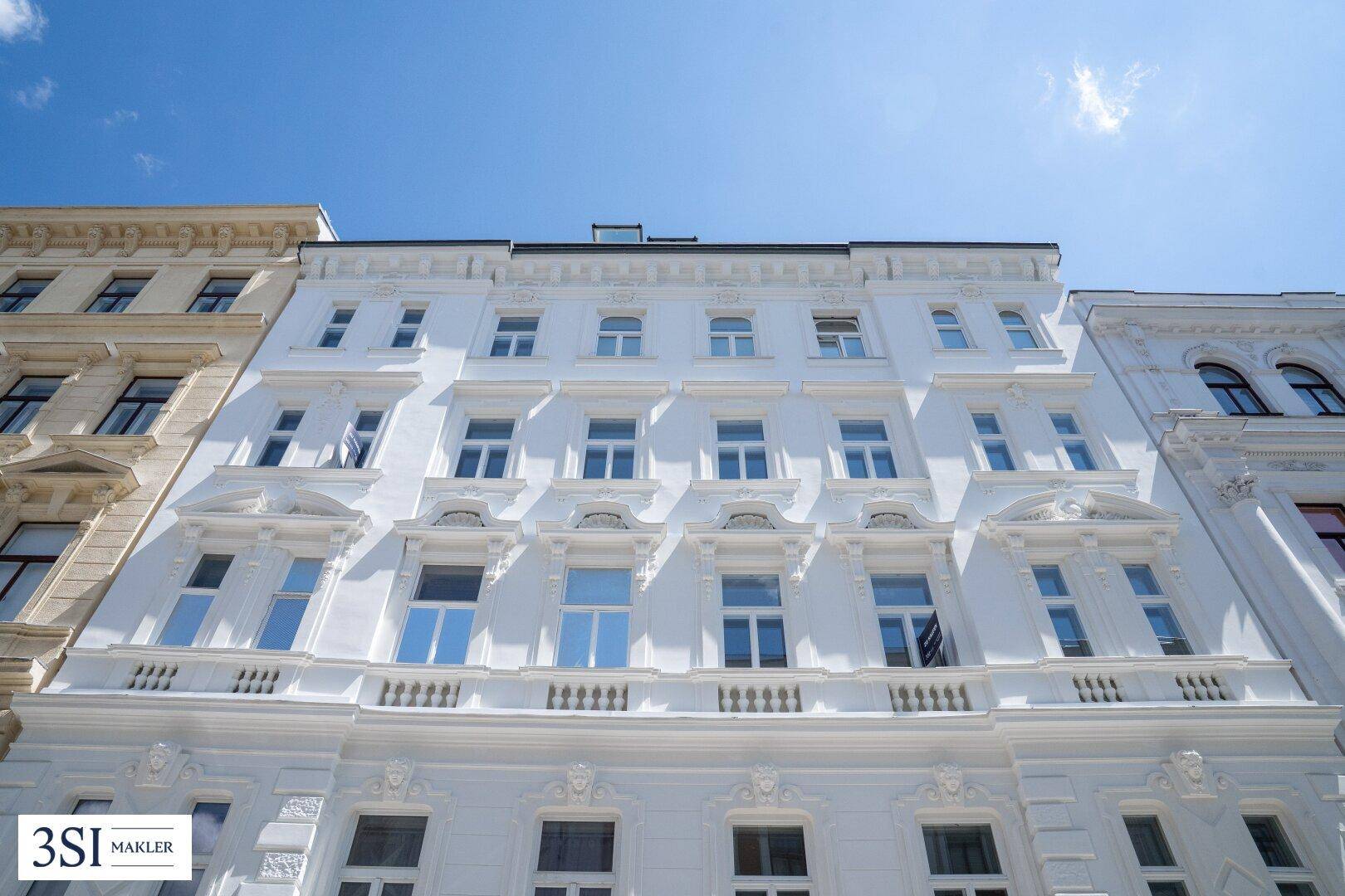 Prächtige, weiße Fassade eines historischen Gebäudes mit vielen Fenstern und Stuckelementen.