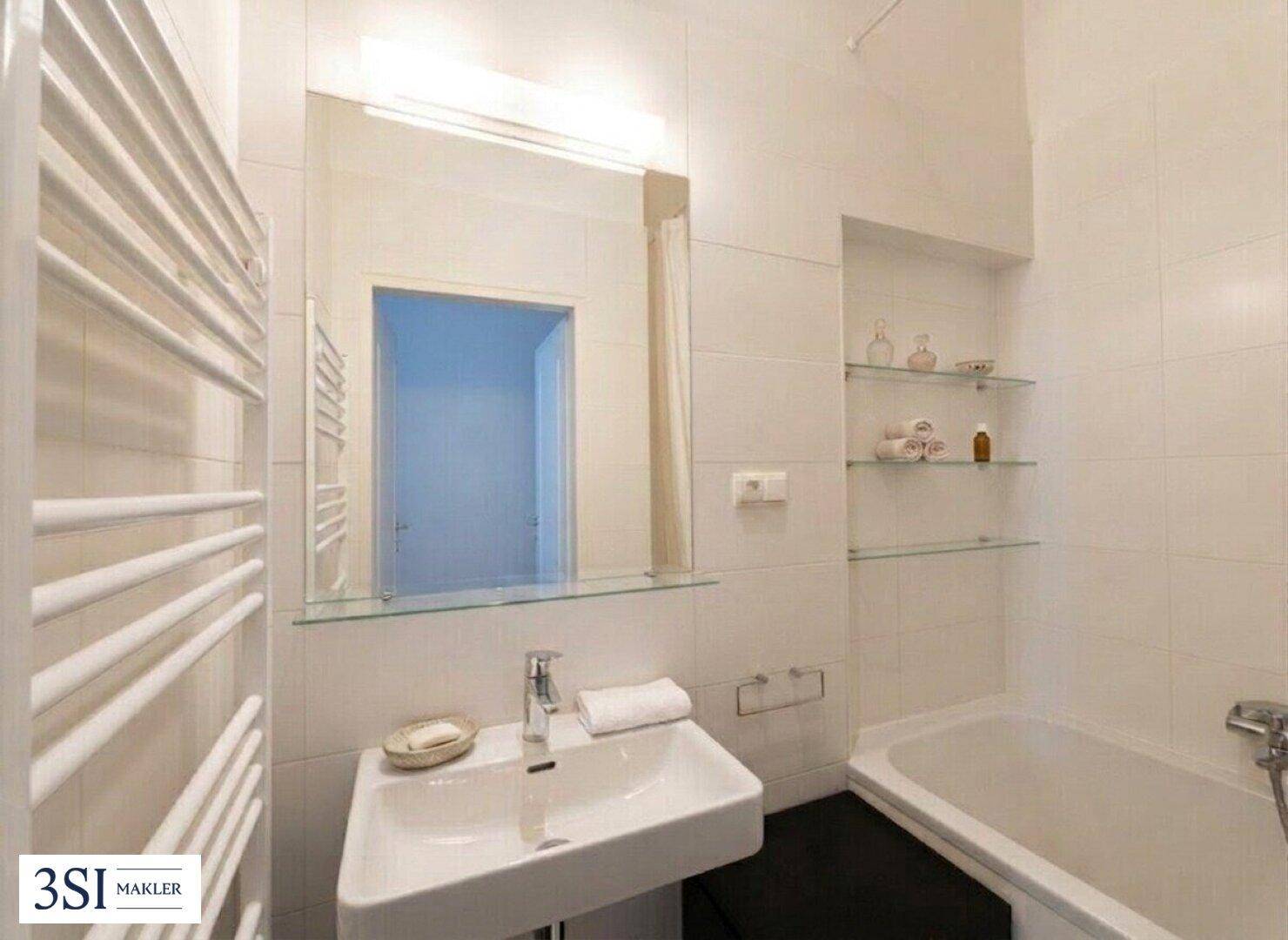 Modernes Badezimmer mit weißen Fliesen, Badewanne, Waschbecken und beheiztem Handtuchhalter.