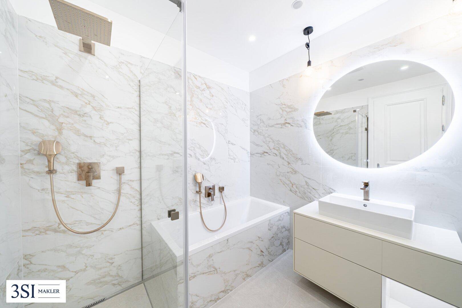 Luxuriöses Badezimmer mit Marmorfliesen, Badewanne, begehbarer Dusche und beleuchtetem Spiegel.
