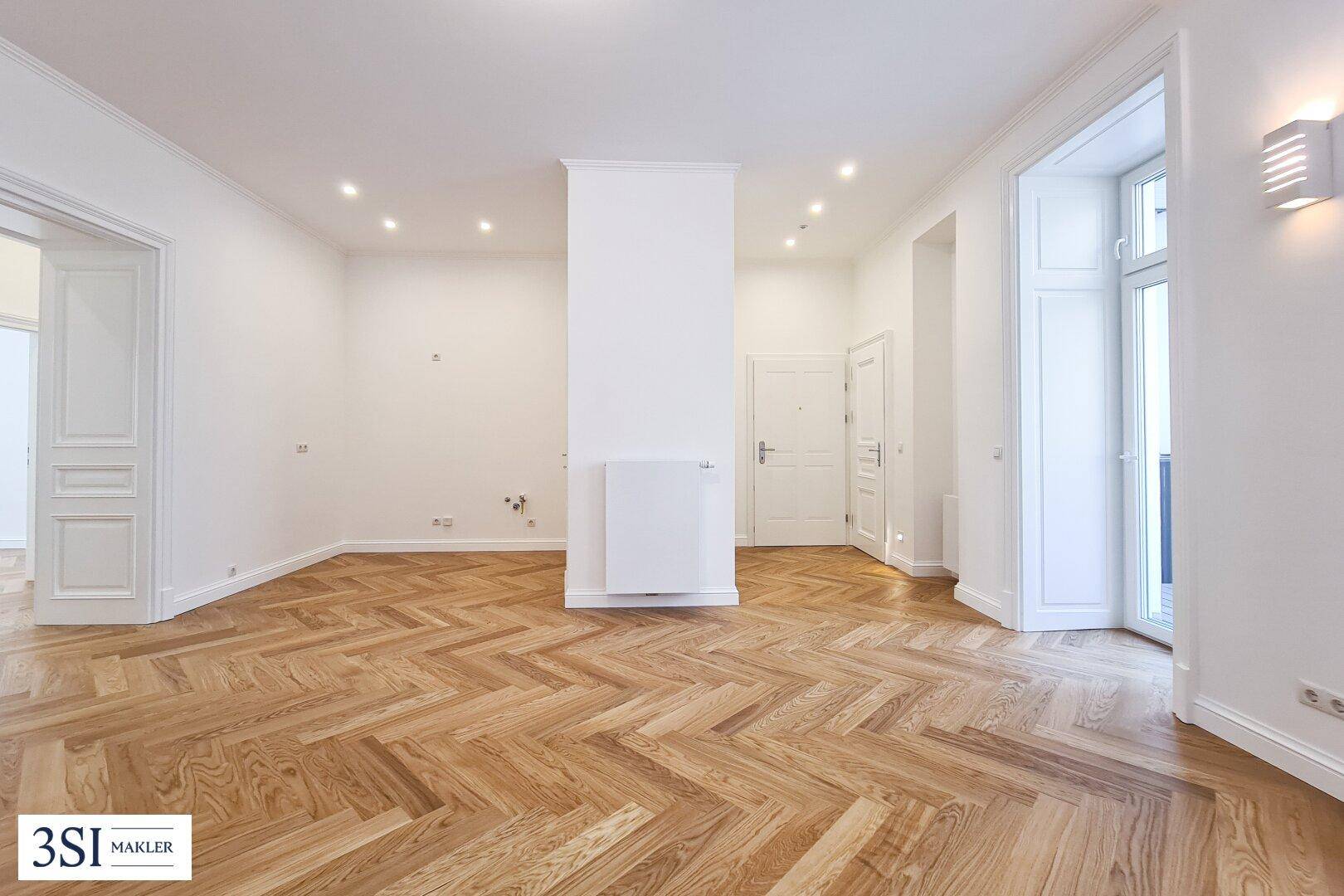 Geräumiges Zimmer mit Fischgrätparkett, weißen Wänden und Zugang zu einem Balkon.