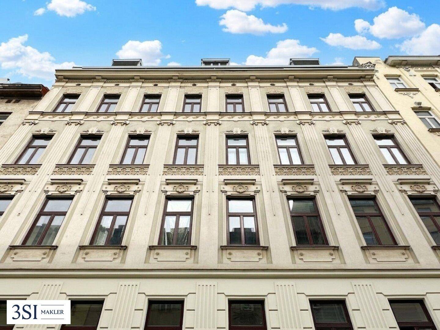 Eindrucksvolle Fassade eines gepflegten Altbaus mit dekorativen Elementen und braunen Fenstern unter blauem Himmel.