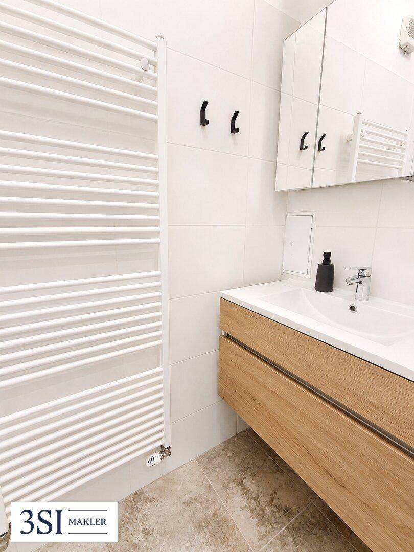 Modernes Badezimmer mit Holzwaschtisch, Spiegelkabinett und weißem Handtuchheizkörper.