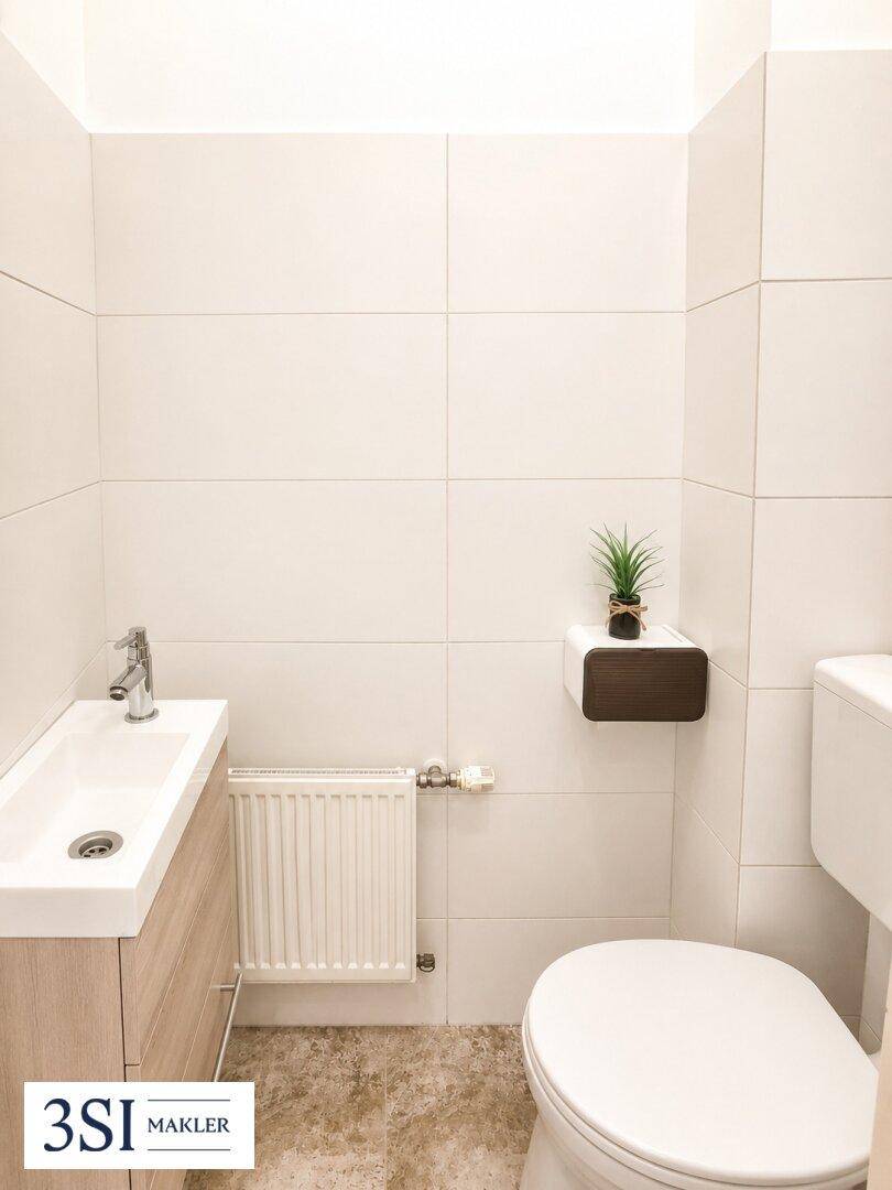 Separates WC mit kleinem Waschbecken und modernen Fliesen in hellem Design.