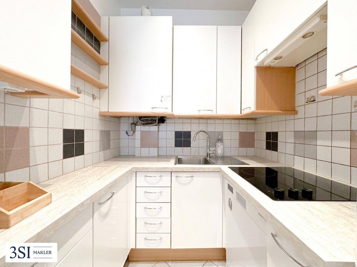 Kleine, funktionale Küche mit weißen Schränken, Fliesenrückwand und Induktionskochfeld.