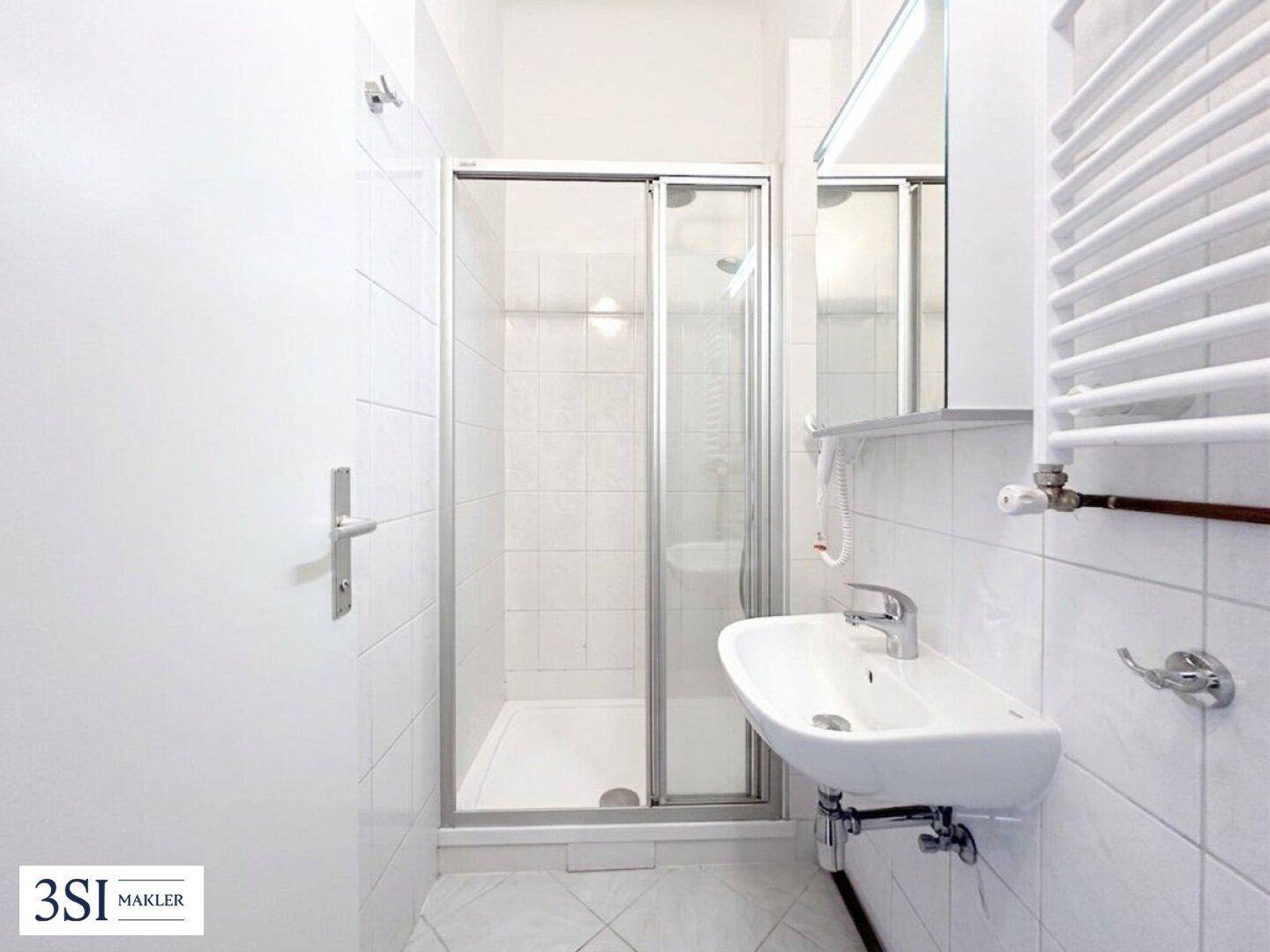 Helles Badezimmer mit Duschkabine, Waschbecken und beheiztem Handtuchhalter.