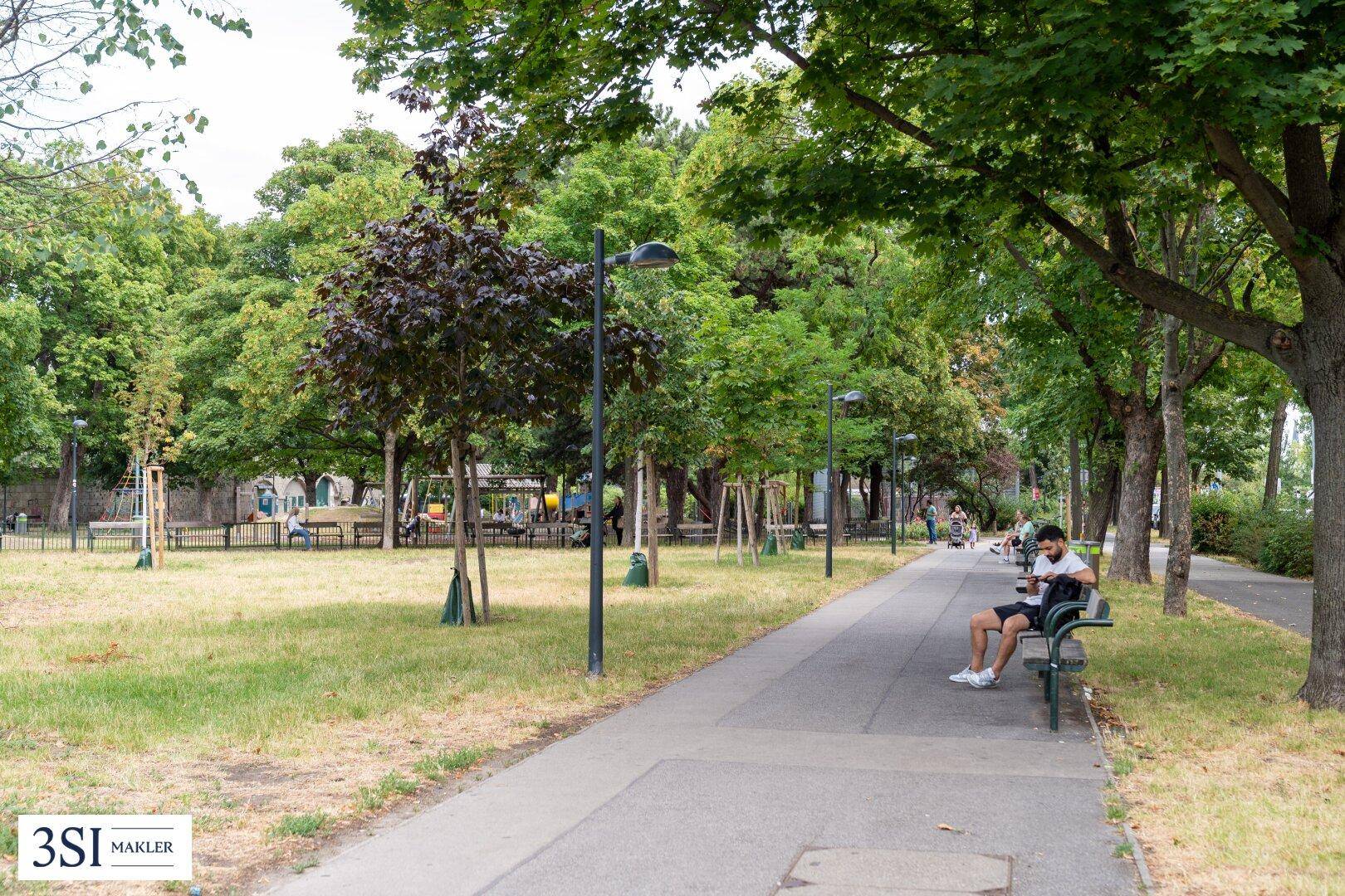 Ein grüner Parkbereich mit Spazierwegen, Bänken und vielen Bäumen, ideal zur Erholung.