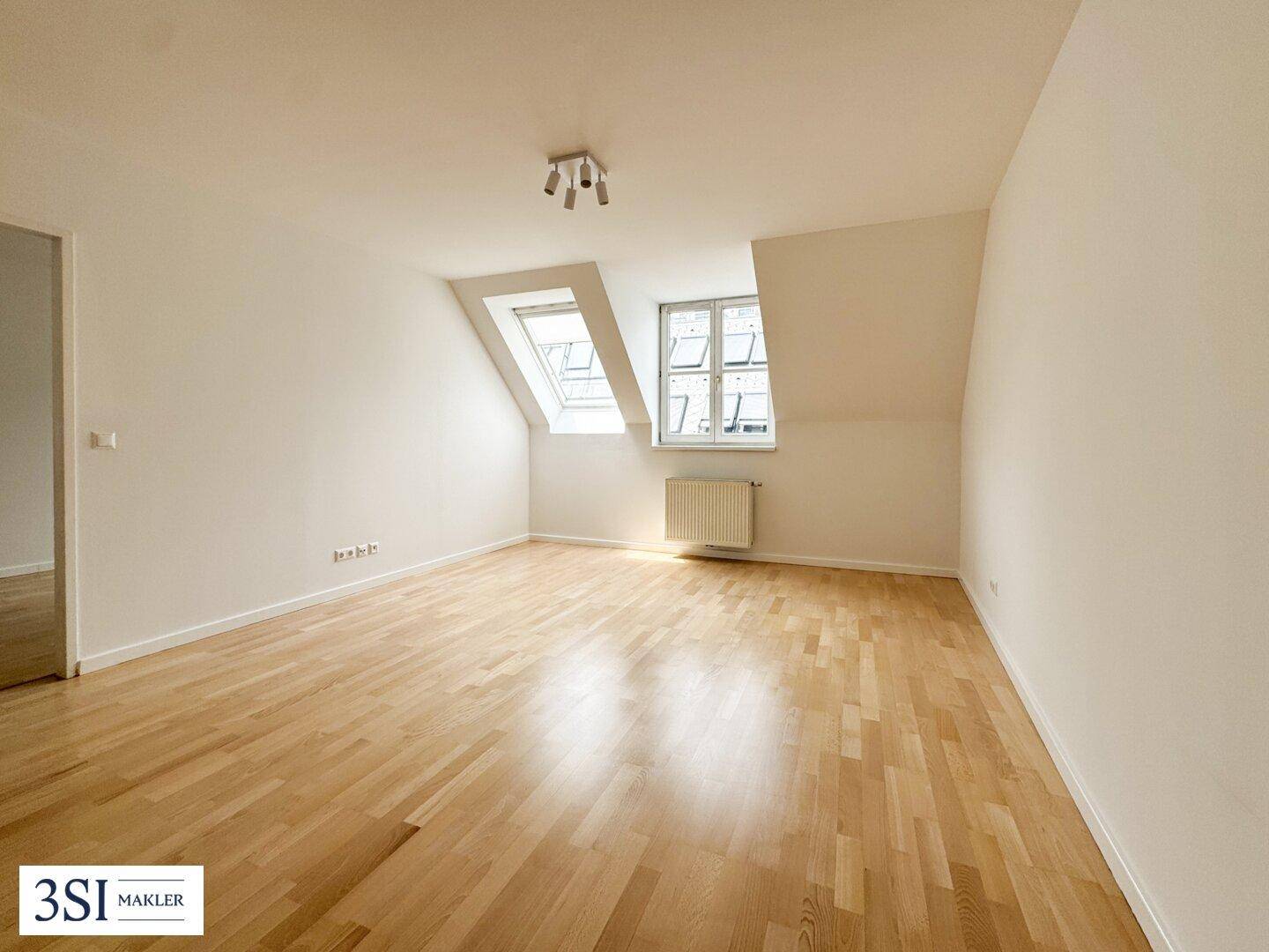 Heller Raum im Dachgeschoss mit Holzboden, Dachfenstern und einem Heizkörper.