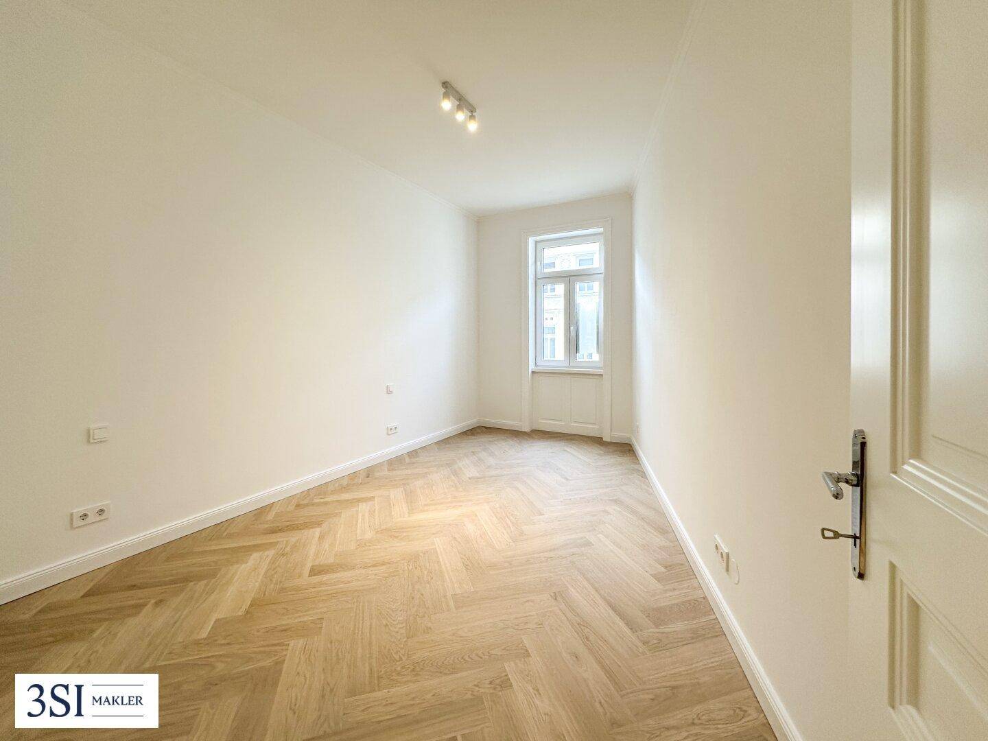 Kleineres, helles Zimmer mit einem Fenster und Fischgrätparkett, perfekt als Kinder- oder Gästezimmer.
