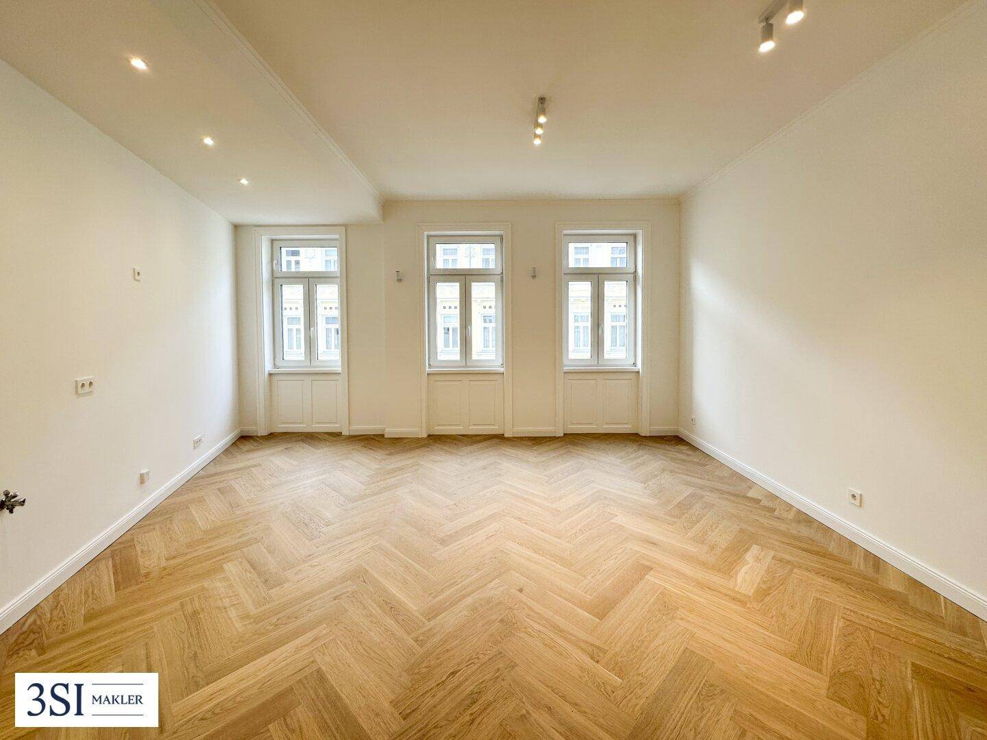 Geräumiger, leerer Raum mit Fischgrätparkett und drei großen Fenstern, bereit zur individuellen Gestaltung.