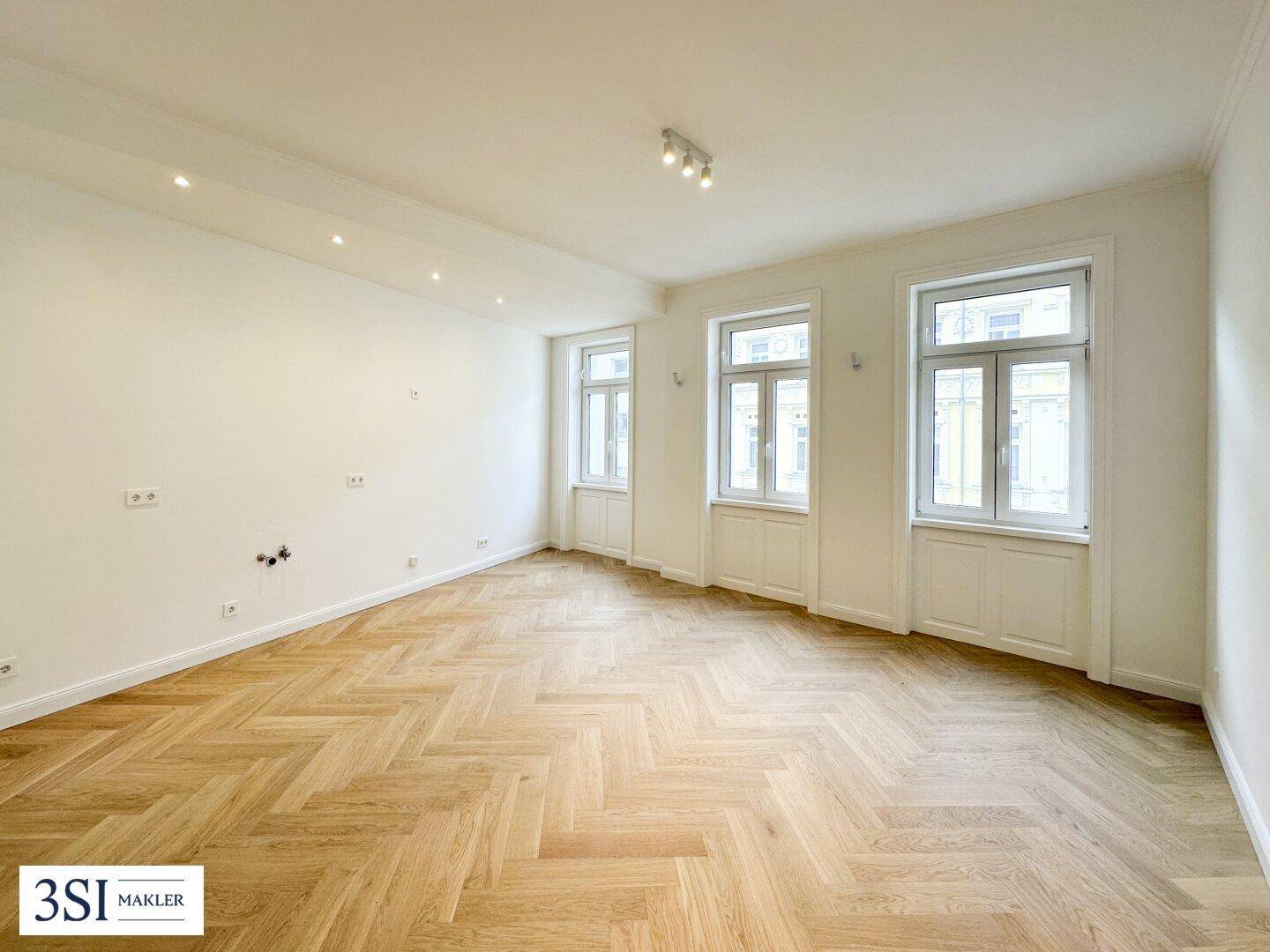 Großer, heller Raum mit Fischgrätparkett und drei hohen Fenstern, vielseitig nutzbar.