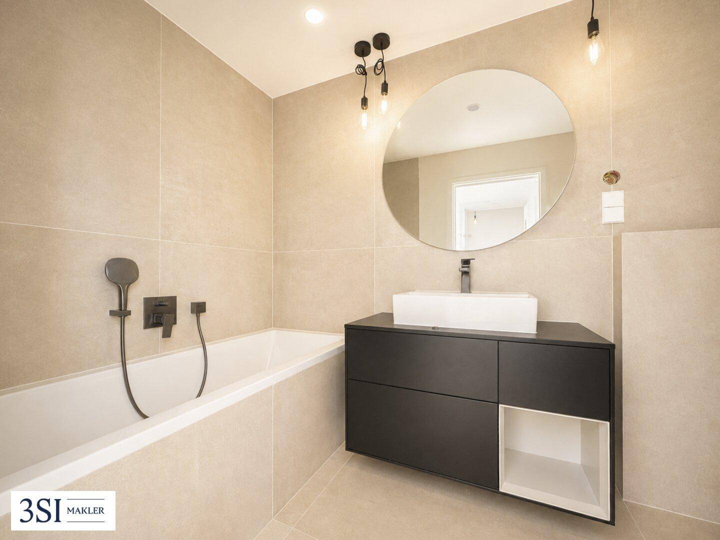 Modernes Badezimmer mit beigefarbenen Fliesen, integrierter Badewanne und stilvollem Waschtisch mit rundem Spiegel.