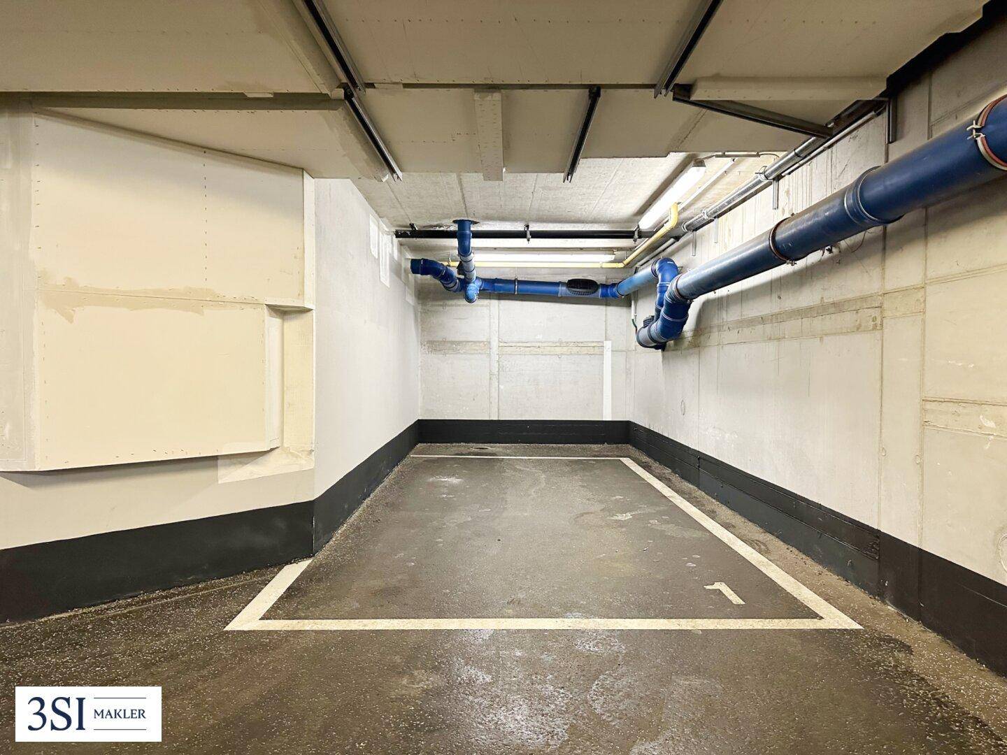 Tiefgaragenstellplatz mit klaren Markierungen und sichtbaren Installationen an der Decke des Gebäudes.