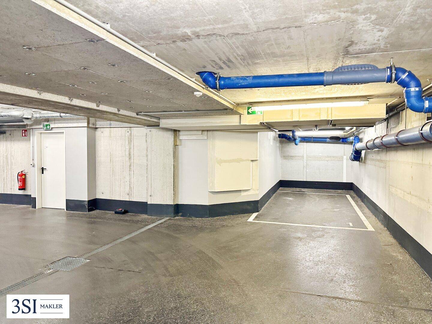 Tiefgarage mit mehreren Stellplätzen, Betonwänden und blauen Rohren an der Decke des Gebäudes.