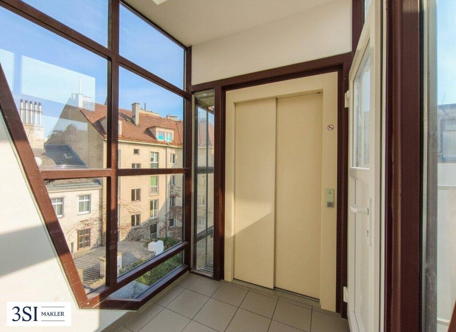 Moderner Aufzugsbereich mit großen Fenstern, die einen Blick auf den Innenhof freigeben.