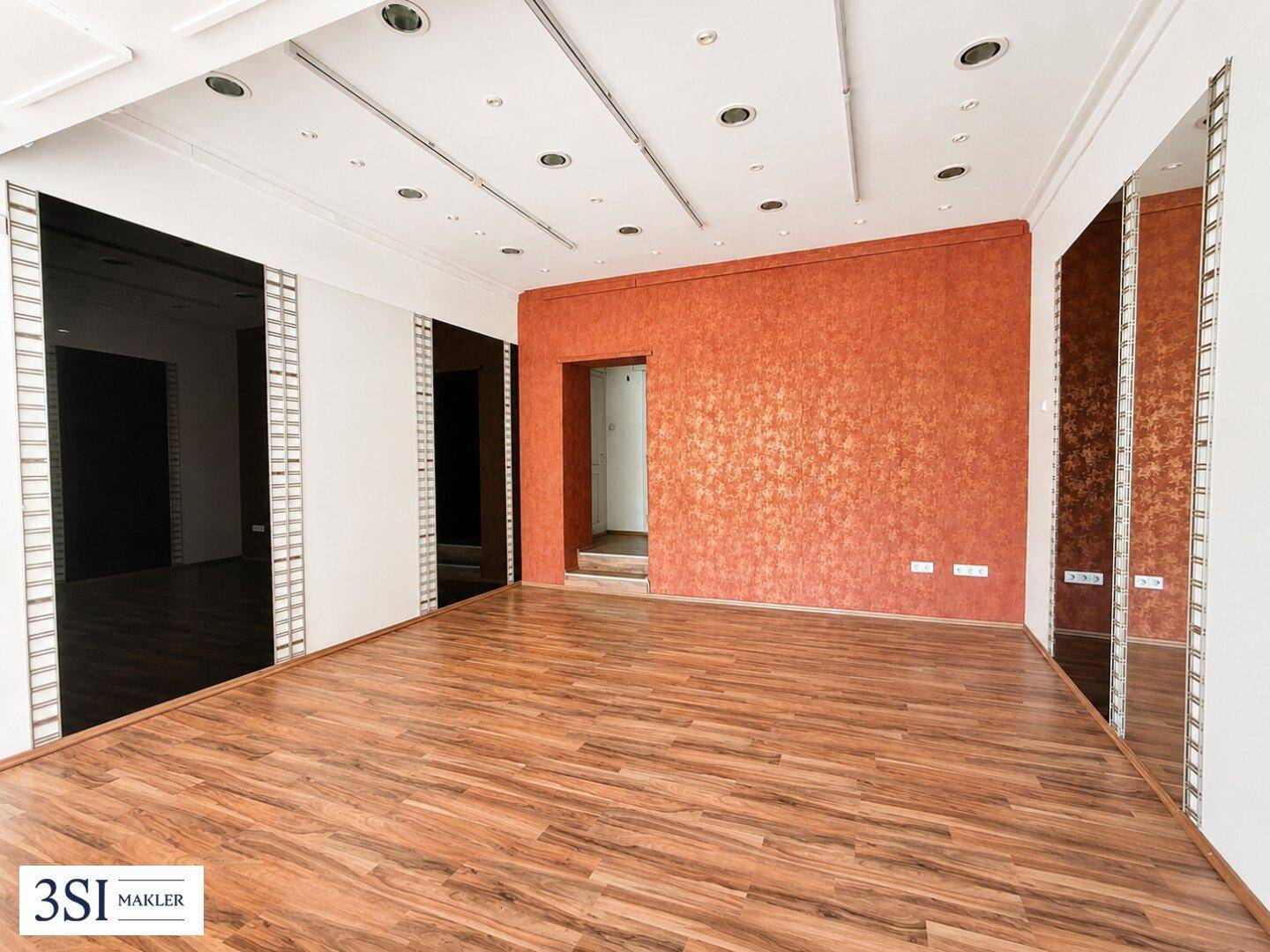 Innenansicht eines Geschäftsraums mit auffälliger orangeroter Wand, Laminatboden und Deckenbeleuchtung.