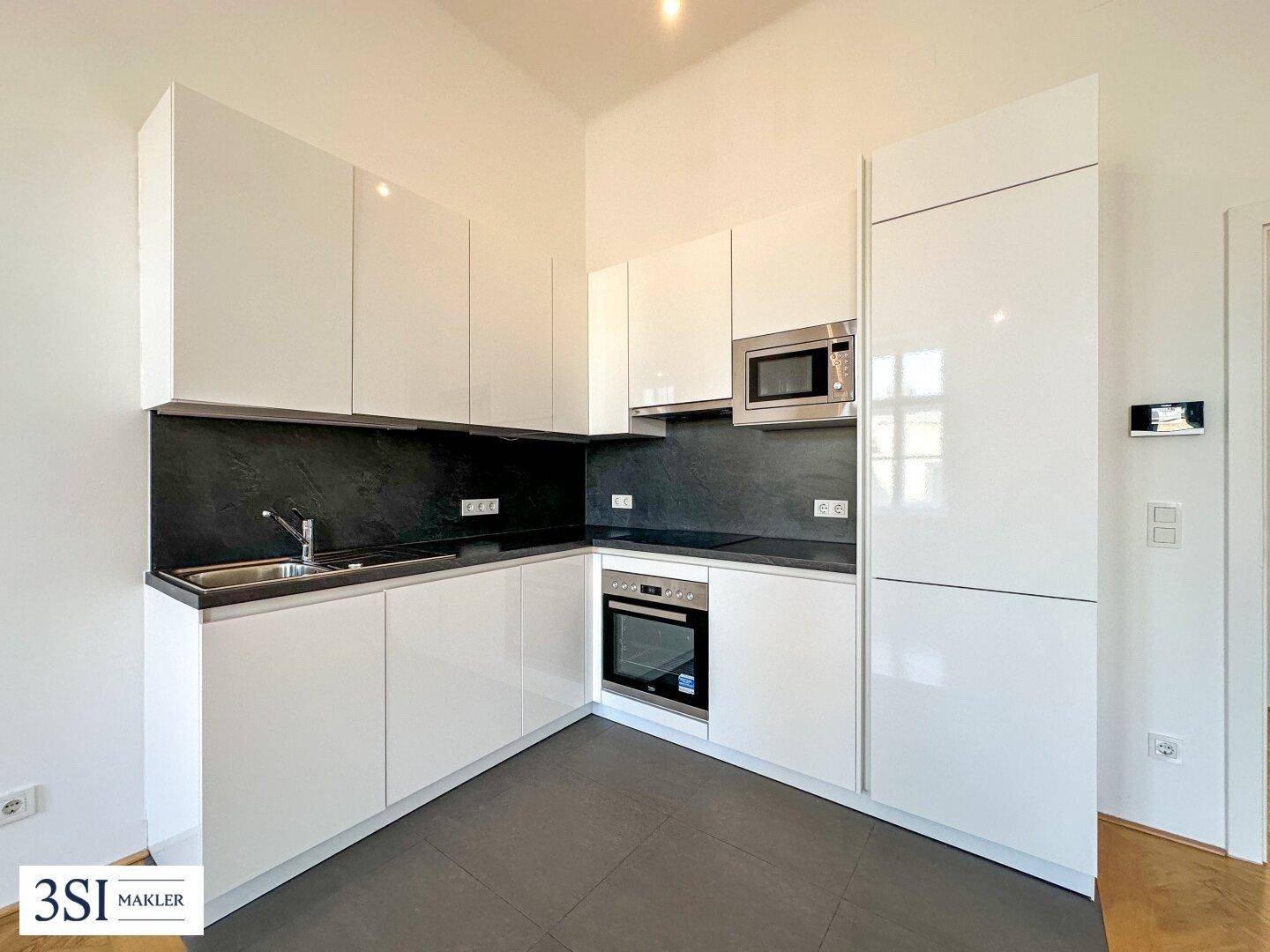 Moderne Einbauküche mit weißen Hochglanzfronten, dunkler Arbeitsplatte und integrierten Geräten.