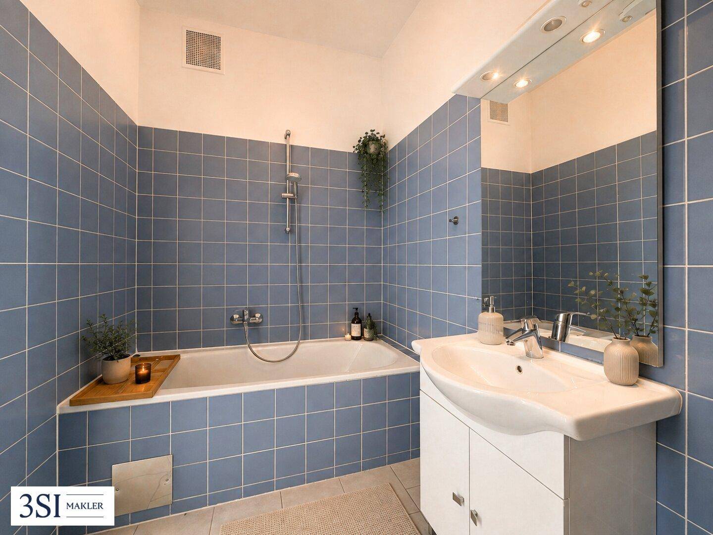 Badezimmer mit blauen Fliesen, Badewanne und Waschbecken mit Spiegelschrank, bietet grundlegende Ausstattung.