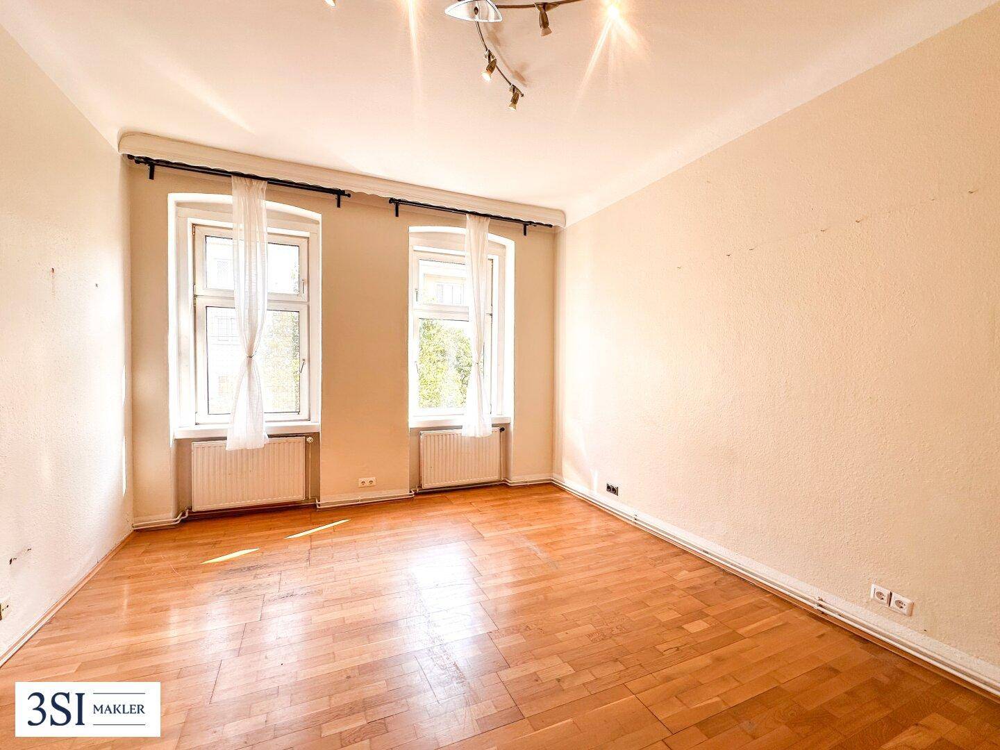 Heller Raum mit Parkettboden und zwei Fenstern, ideal als Wohn- oder Schlafzimmer nutzbar.