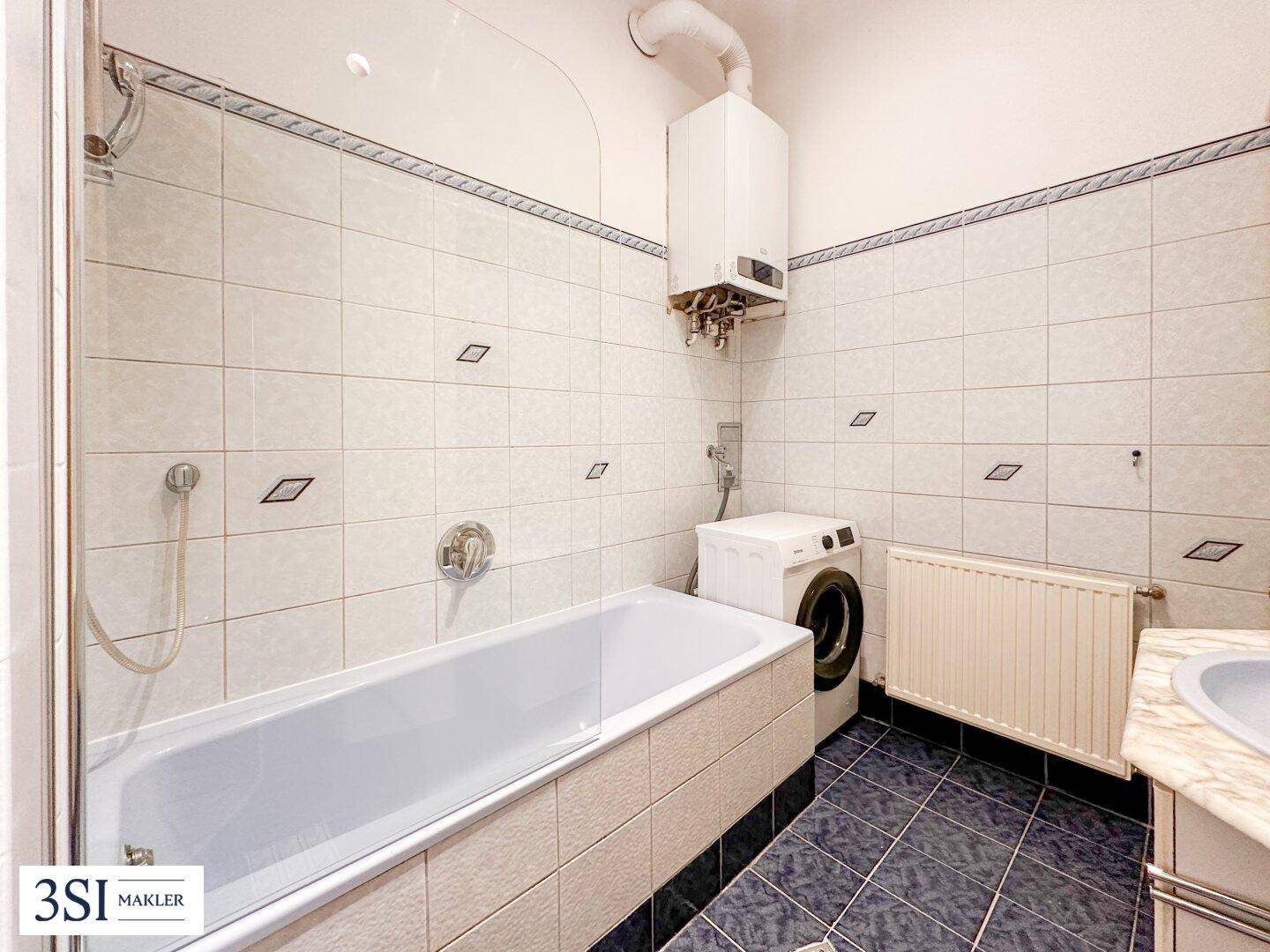 Gefliestes Badezimmer mit Badewanne, Waschbecken und Heizkörper, ausgestattet mit einem Boiler.