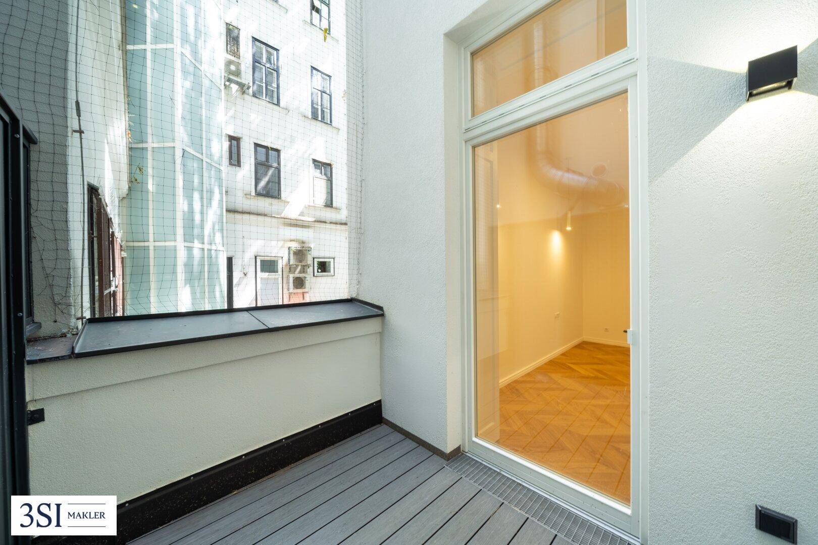 Kleiner Balkon mit Holzoptik-Boden und Blick auf die umliegenden Gebäude.
