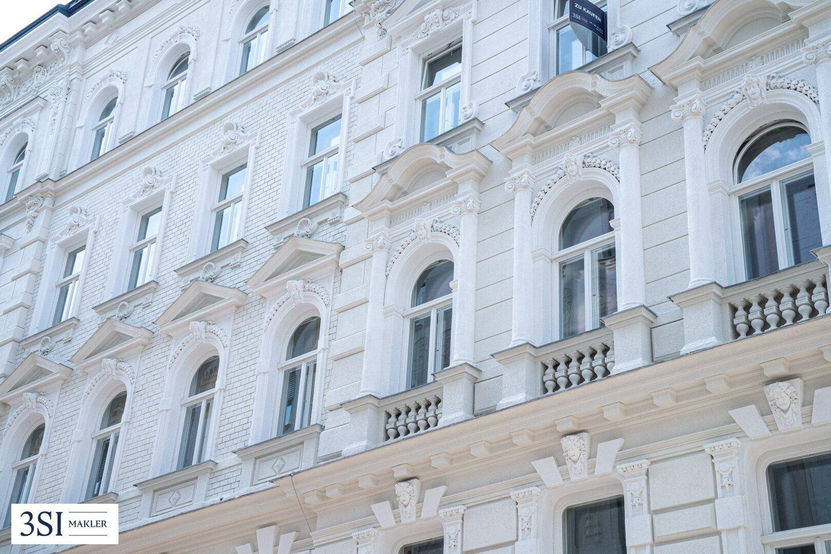 Nahaufnahme der reich verzierten weißen Fassade eines historischen Gebäudes mit Balkonen.