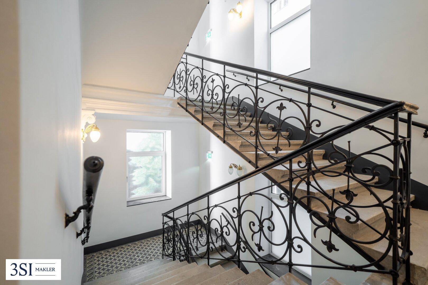 Elegantes Treppenhaus mit kunstvollem schmiedeeisernem Geländer und hellen Stufen in einem Altbau.