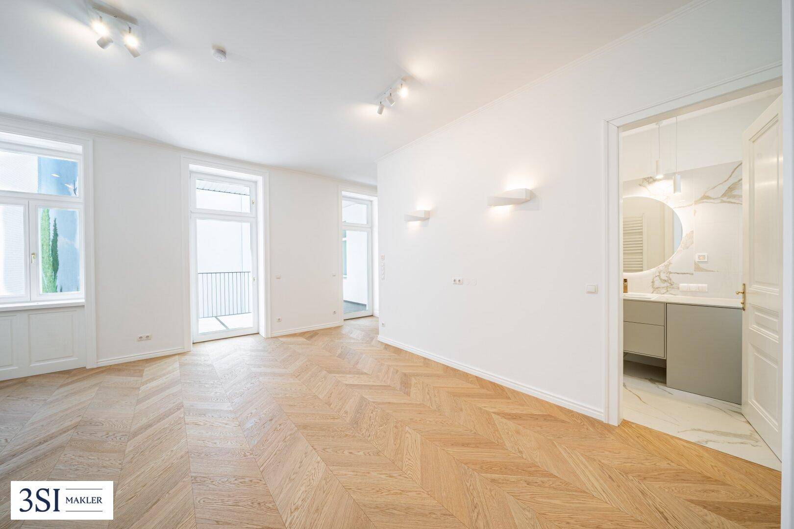 Geräumiges Zimmer mit Fischgrätparkett, Zugang zum Balkon und Blick ins moderne Bad.