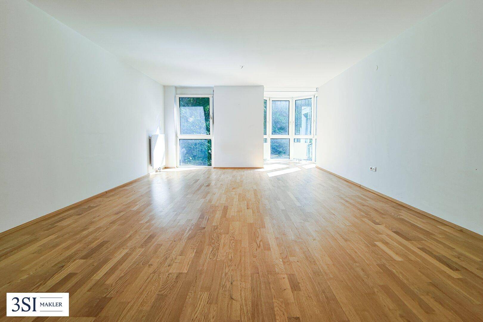 Geräumiges, helles Zimmer mit Holzboden und großen Fenstern, die viel Licht hereinlassen.