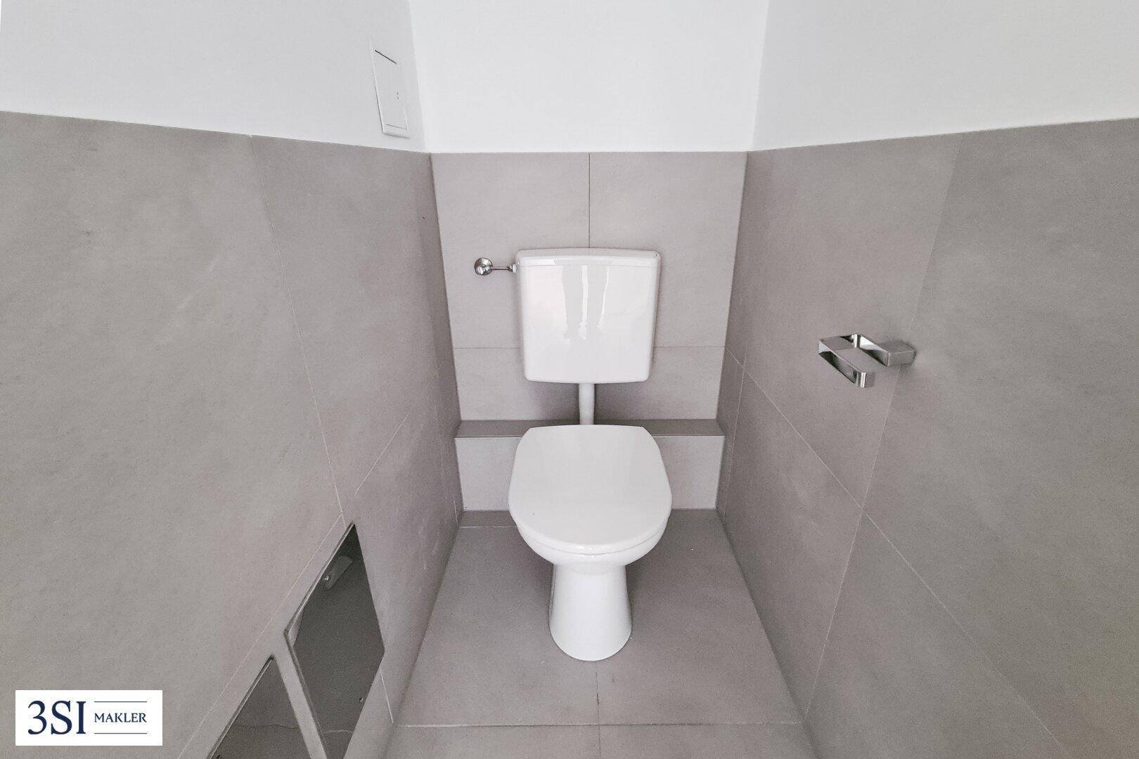 Separates WC mit Wandtoilette und modernen grauen Fliesen.