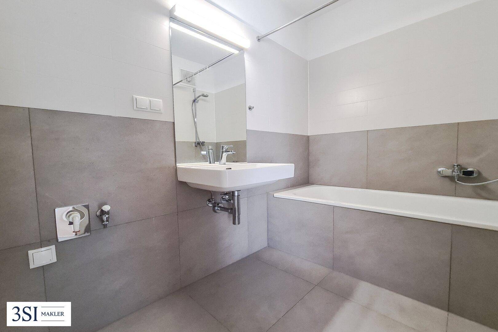 Modernes Badezimmer mit Badewanne, Waschbecken und grauen Fliesen.