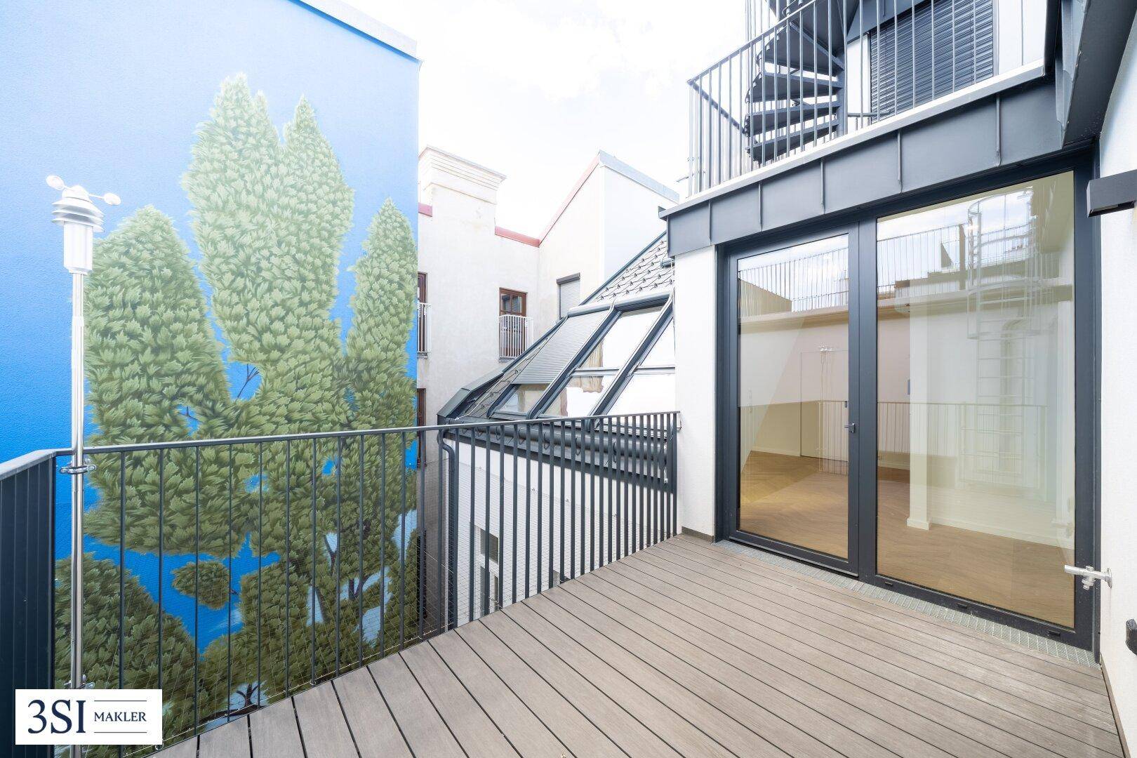 Moderner Balkon mit Holzboden und Blick auf eine bemalte Fassade und eine Wendeltreppe.