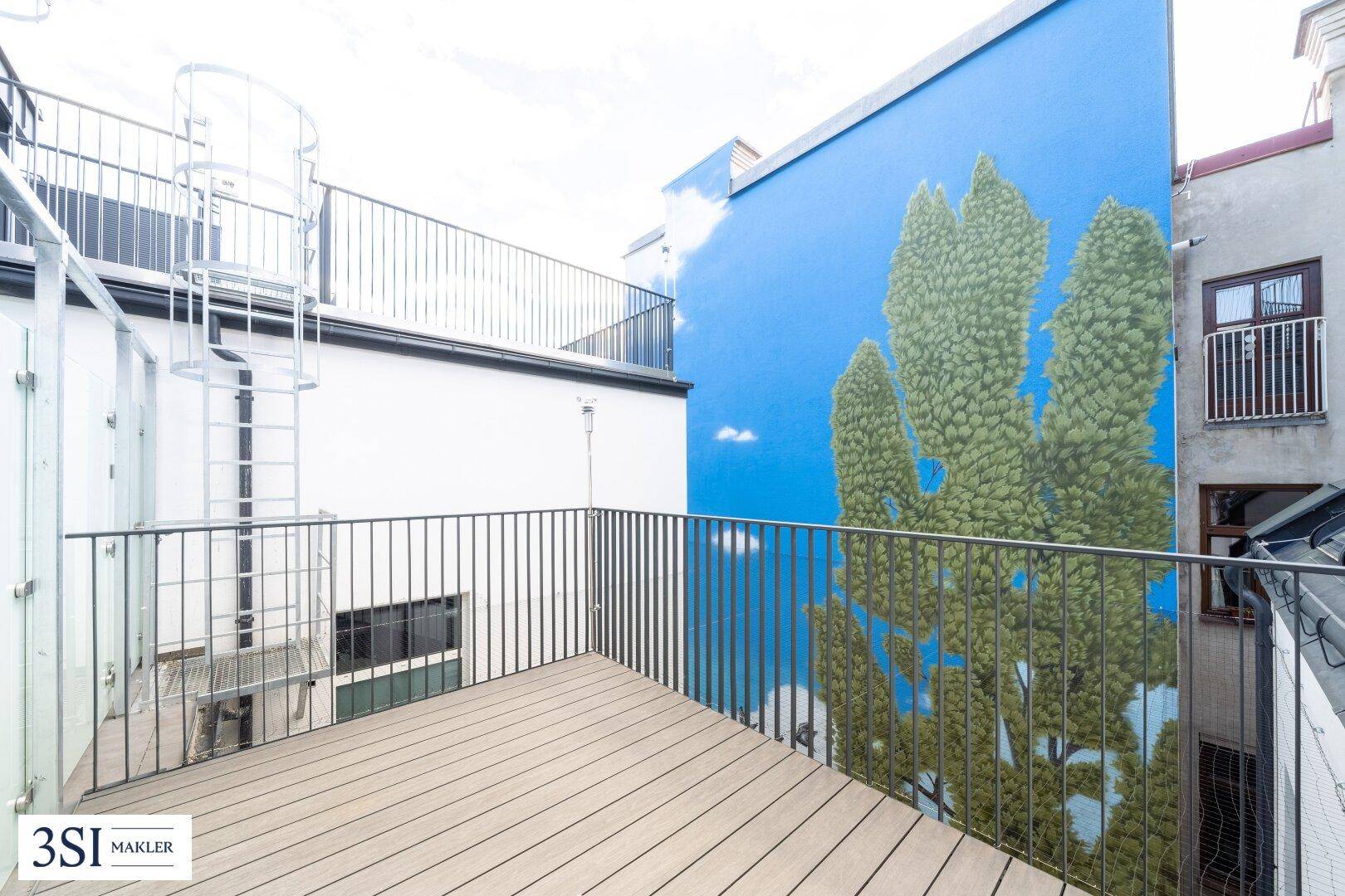 Geräumiger Balkon mit Holzboden, Metallgeländer und einer Wendeltreppe zum oberen Bereich.