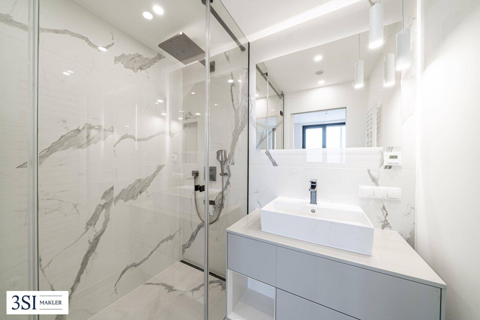 Modernes Badezimmer mit eleganten Marmorfliesen, begehbarer Dusche und stilvollem Einzelwaschbecken.