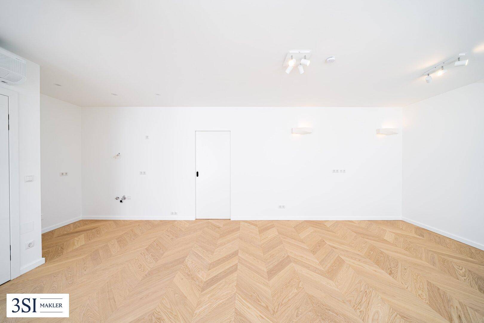 Heller, leerer Raum mit Fischgrätparkett und weißen Wänden, bereit für individuelle Gestaltung.