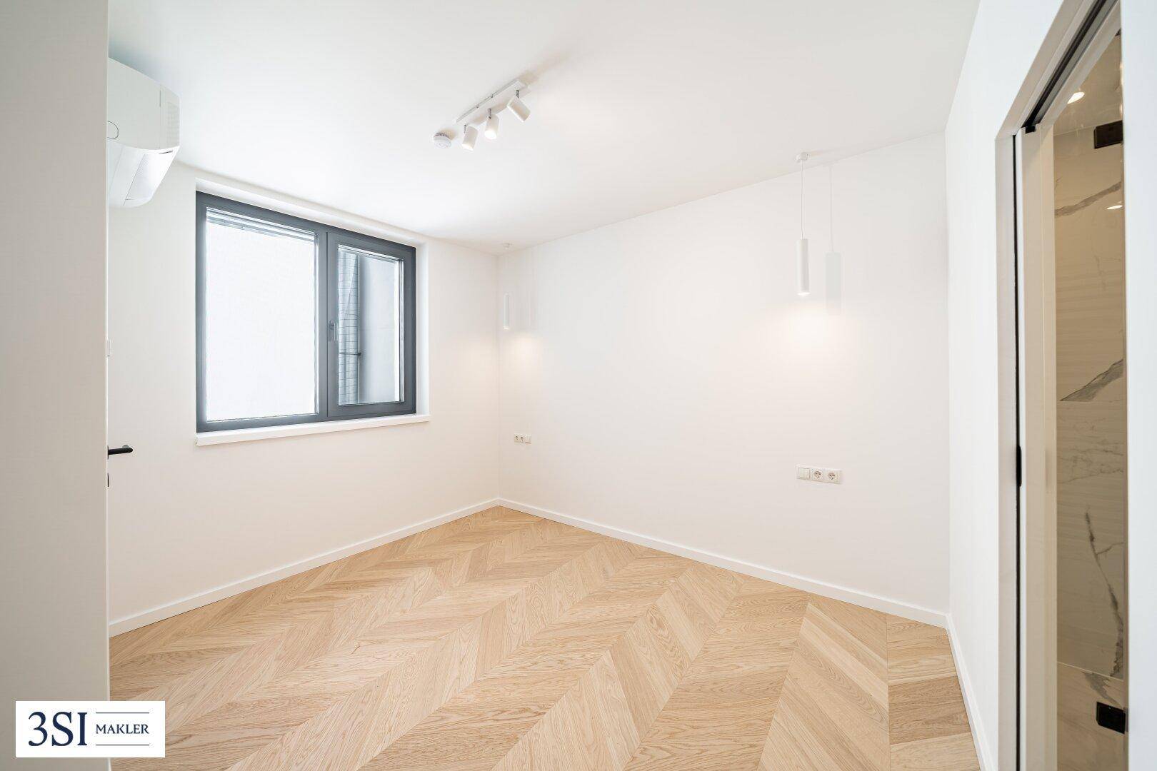 Gemütliches Schlafzimmer mit Fischgrätparkett, einem Fenster und Klimaanlage für angenehmes Raumklima.