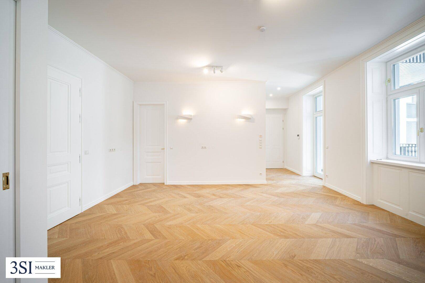 Geräumiges, helles Zimmer mit Fischgrätparkett und mehreren Türen, bereit zur individuellen Gestaltung.