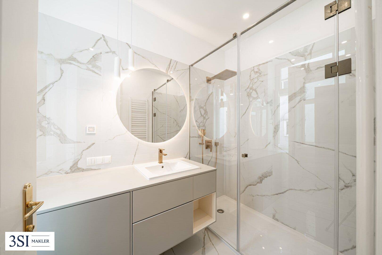 Modernes Badezimmer mit Marmorfliesen, begehbarer Dusche und beleuchtetem Spiegel.