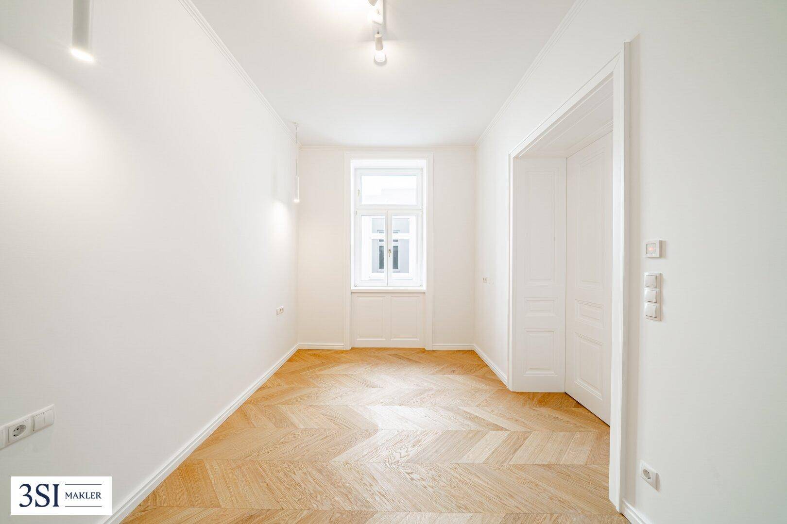 Heller Flur oder kleines Zimmer mit Fischgrätparkett und einem Fenster, frisch renoviert.