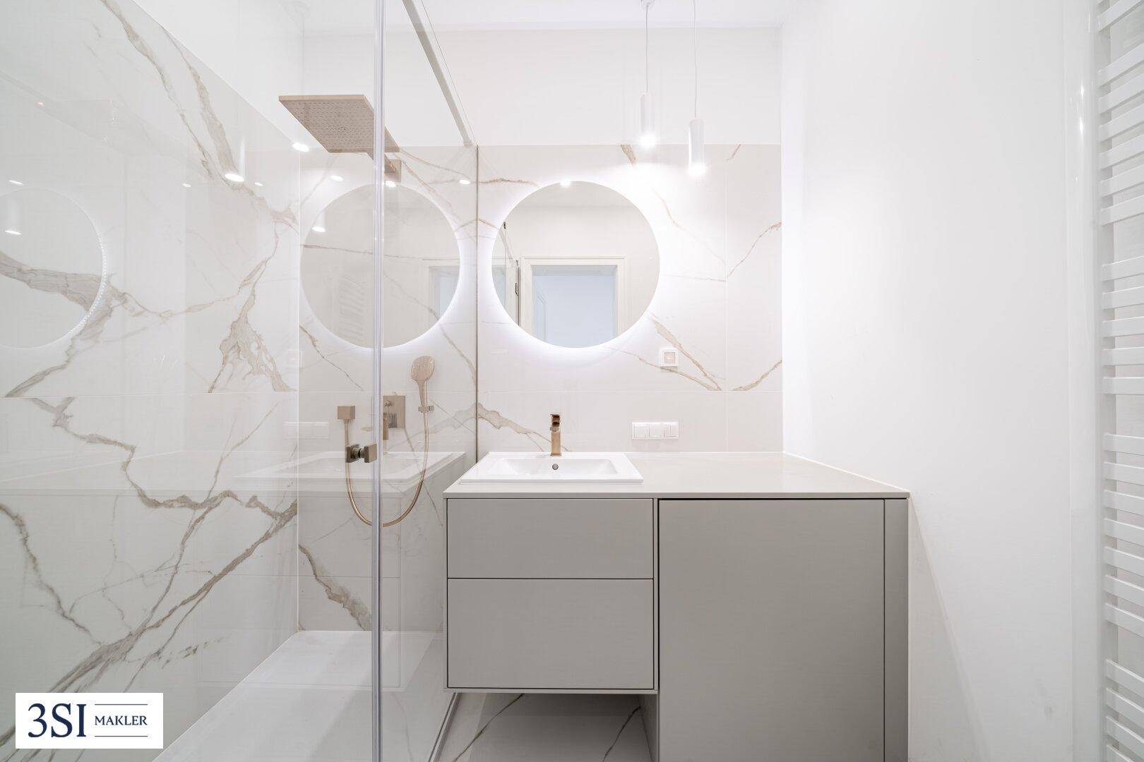 Modernes Badezimmer mit Marmoroptikfliesen, beleuchtetem Spiegel und begehbarer Dusche.