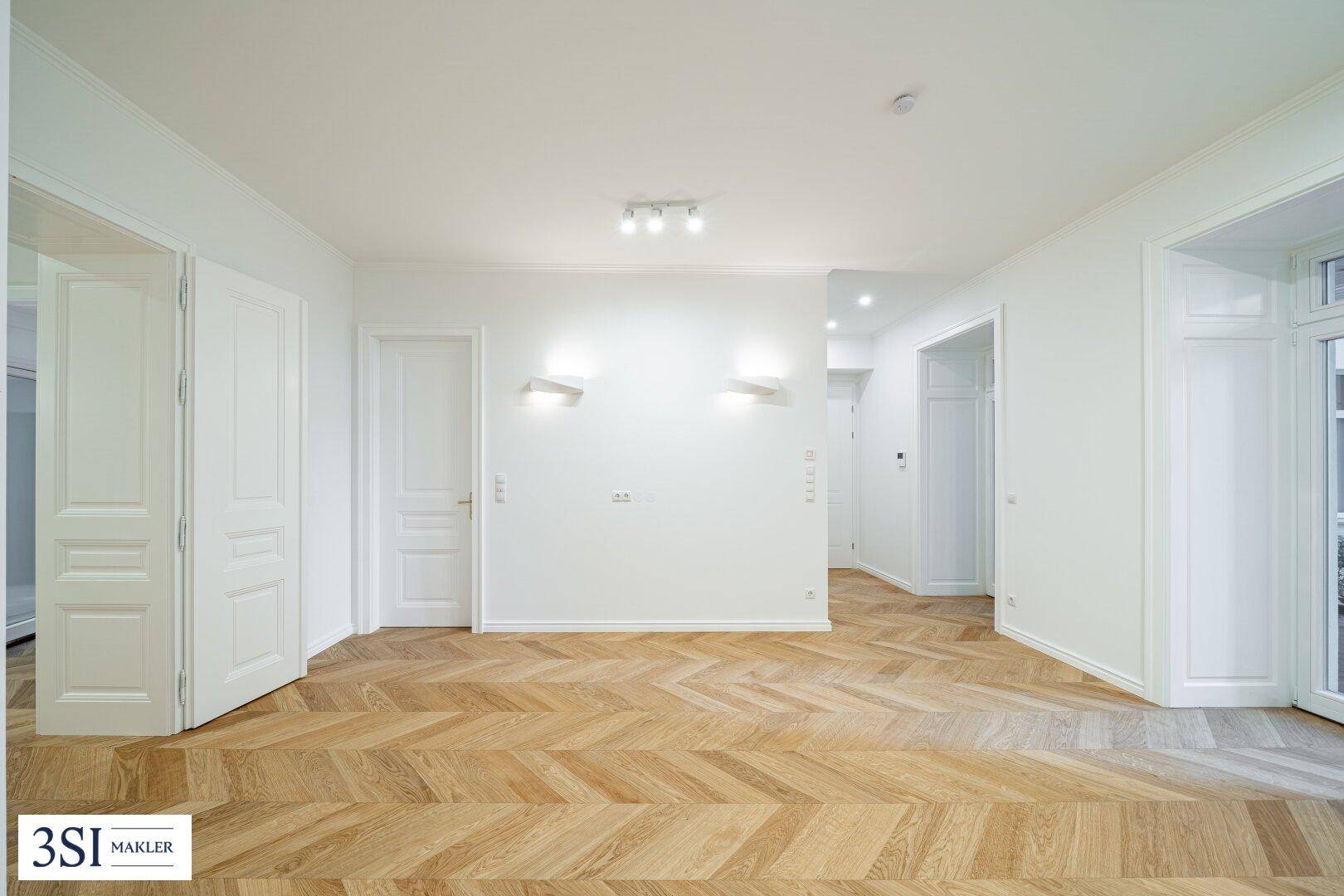 Geräumiges Zimmer mit elegantem Fischgrätparkett und mehreren Türen, bereit zur individuellen Gestaltung.