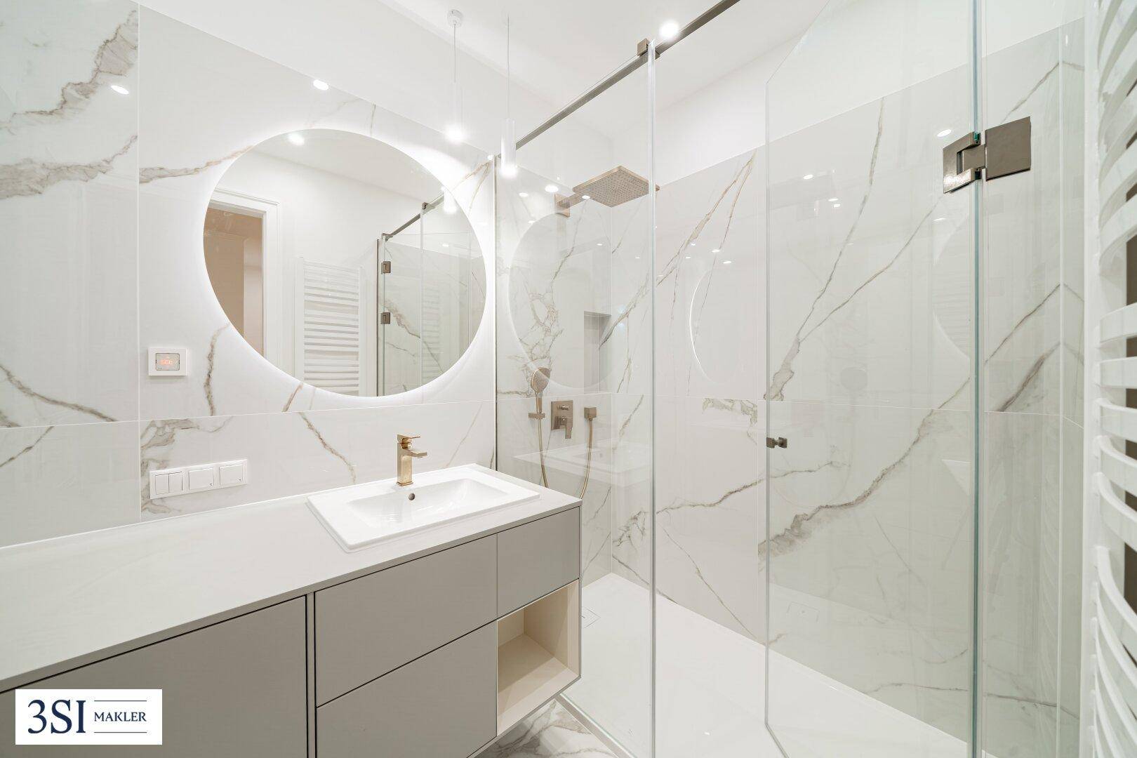 Modernes Badezimmer mit stilvollem Waschtisch, beleuchtetem Spiegel und großer begehbarer Dusche.