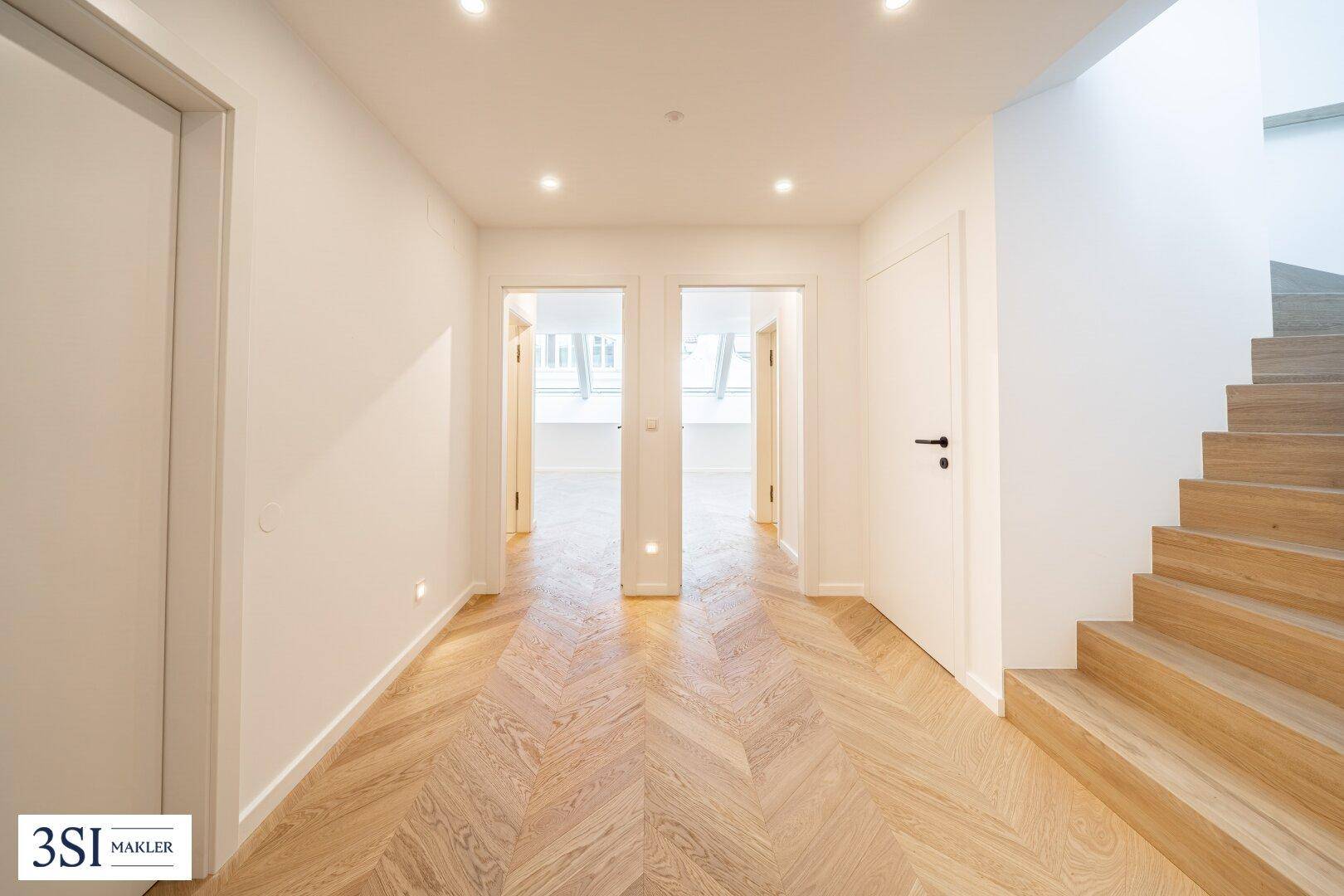 Heller Flur mit elegantem Fischgrätparkett und moderner Holztreppe.