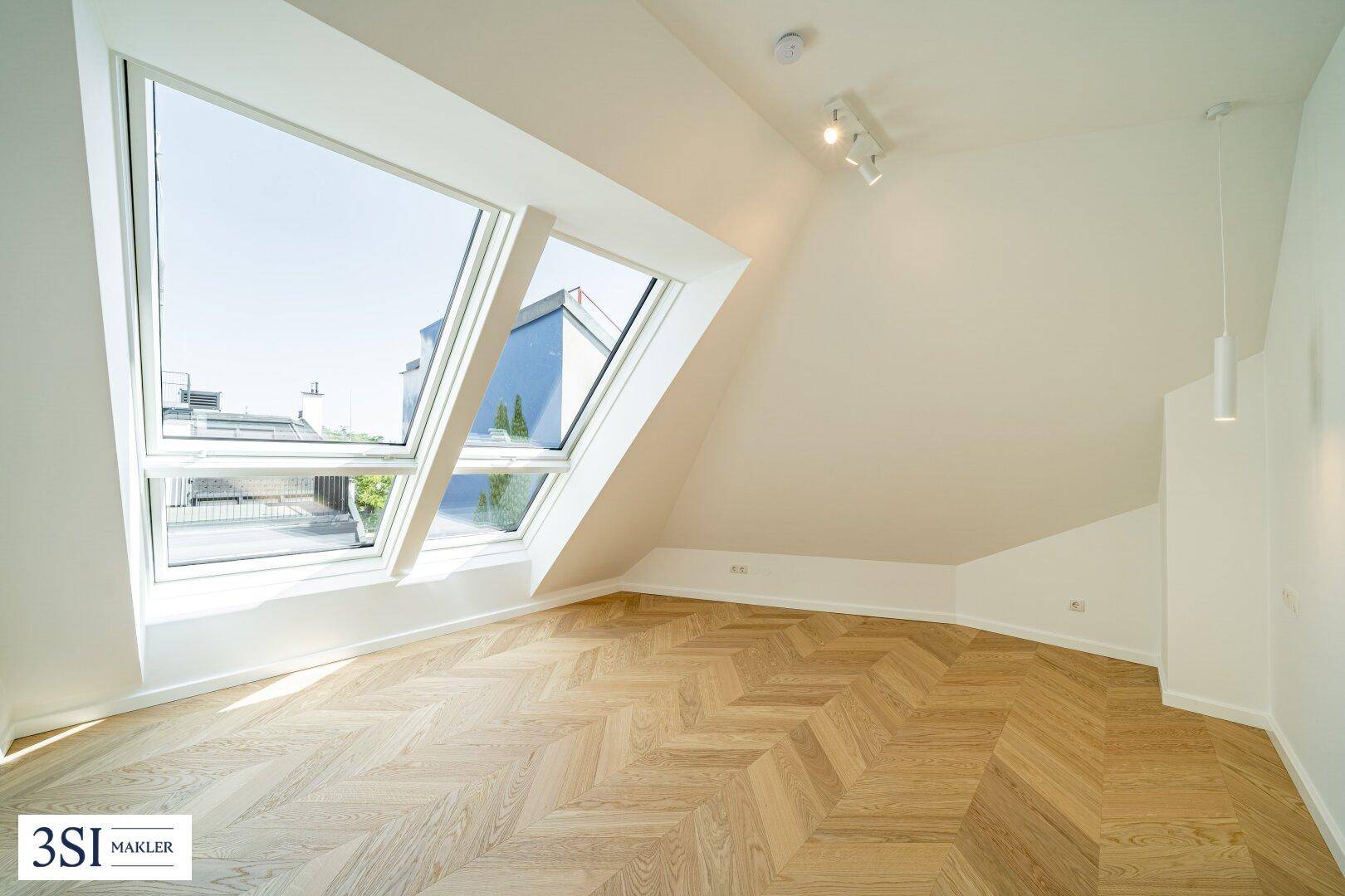 Helles Zimmer mit schrägen Dachfenstern und Fischgrätparkett, ideal als Schlaf- oder Arbeitszimmer.