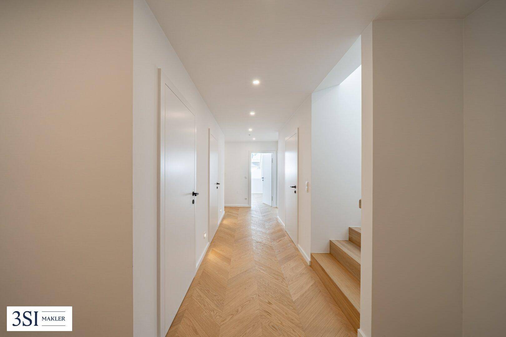 Heller Flur mit Fischgrätparkett, Einbaustrahlern und Treppenzugang in einem modernen Neubau.