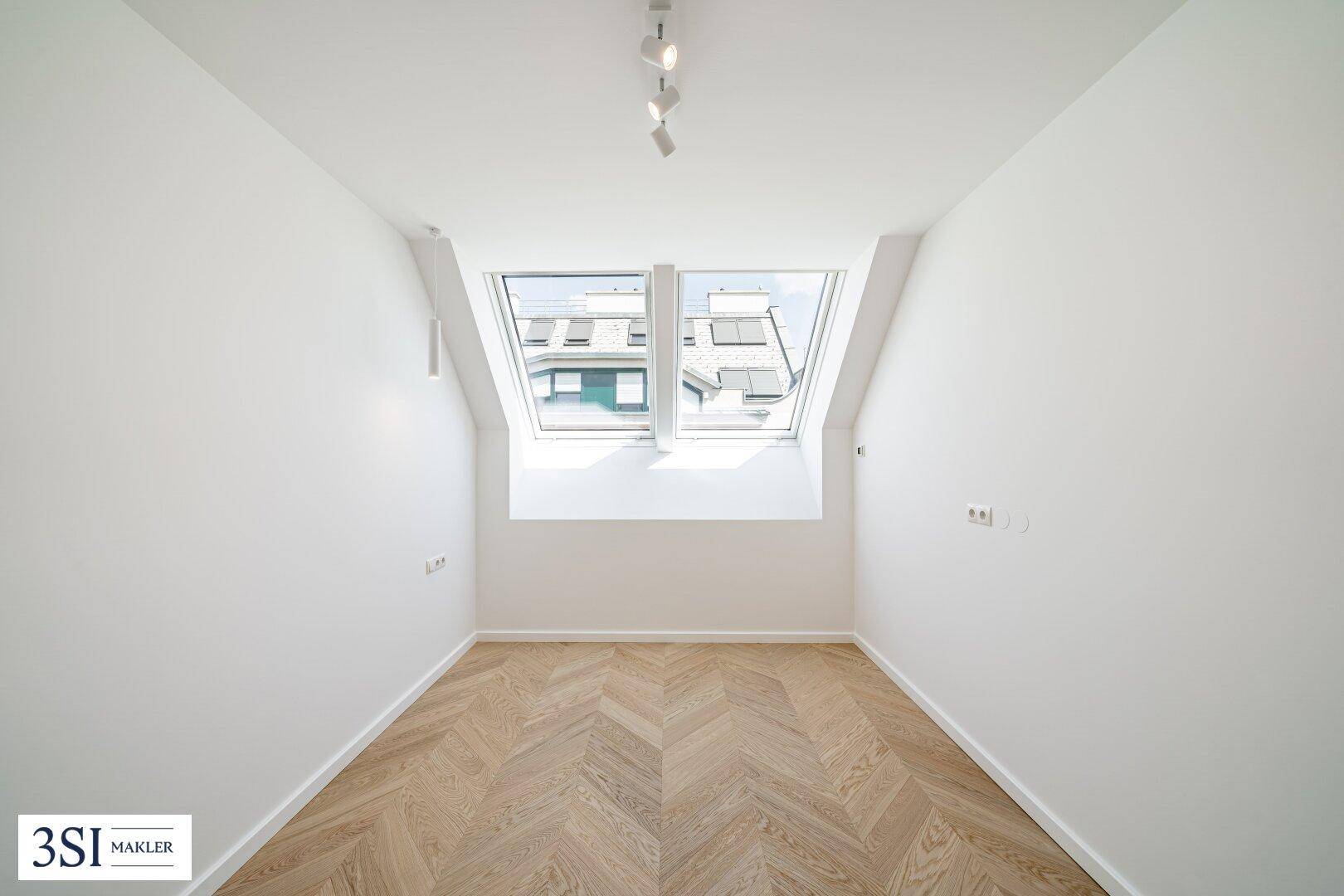 Kleineres Zimmer im Dachgeschoss mit zwei Dachfenstern und hellem Fischgrätparkettboden.
