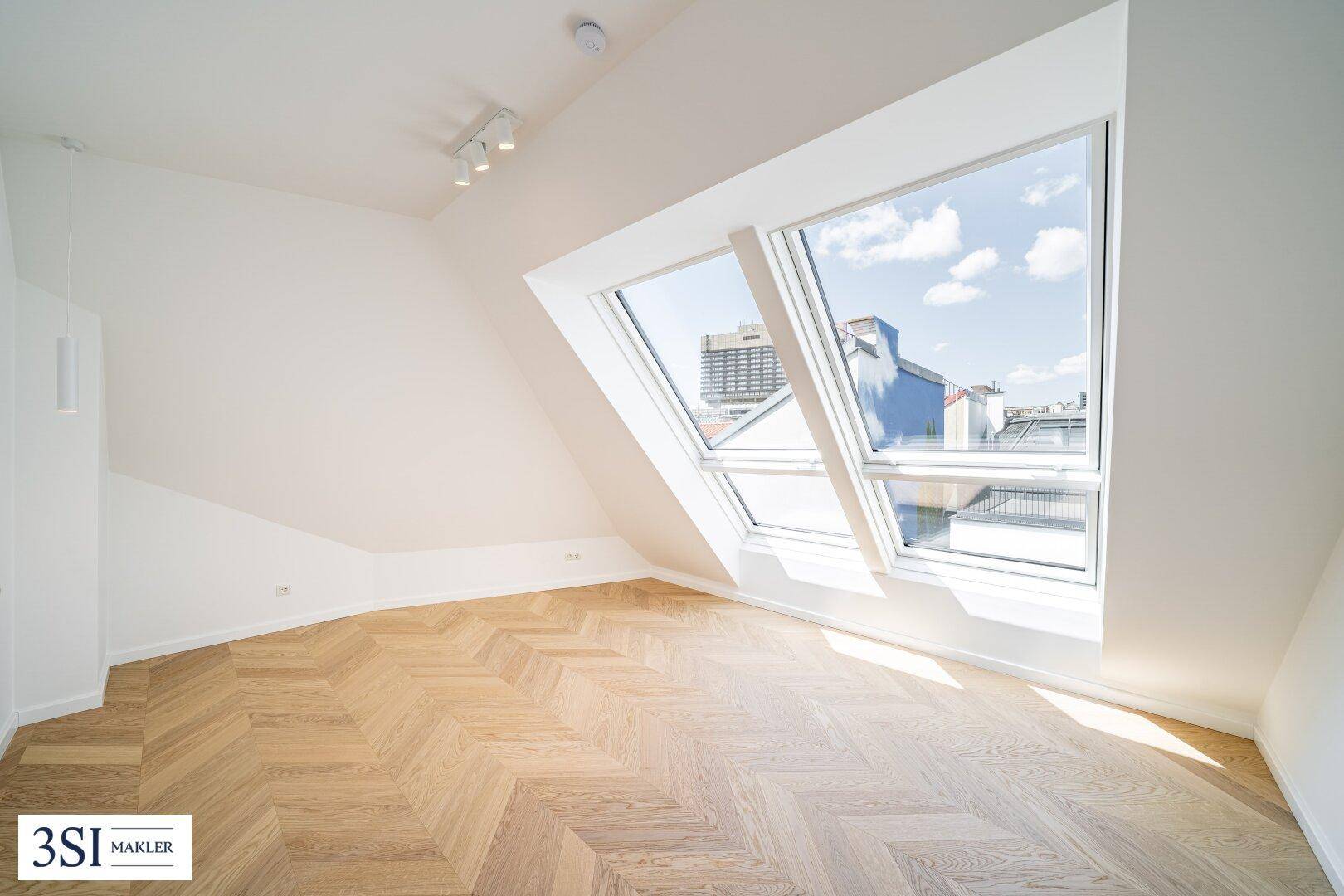 Geräumiges Dachgeschosszimmer mit Fischgrätparkett und großen Dachfenstern mit Stadtblick.