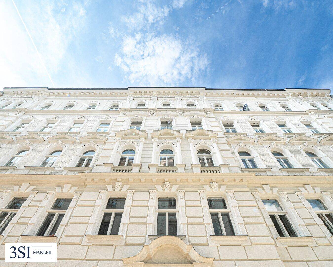 Historische Fassade eines Gebäudes mit vielen Fenstern und dekorativen Elementen unter blauem Himmel.