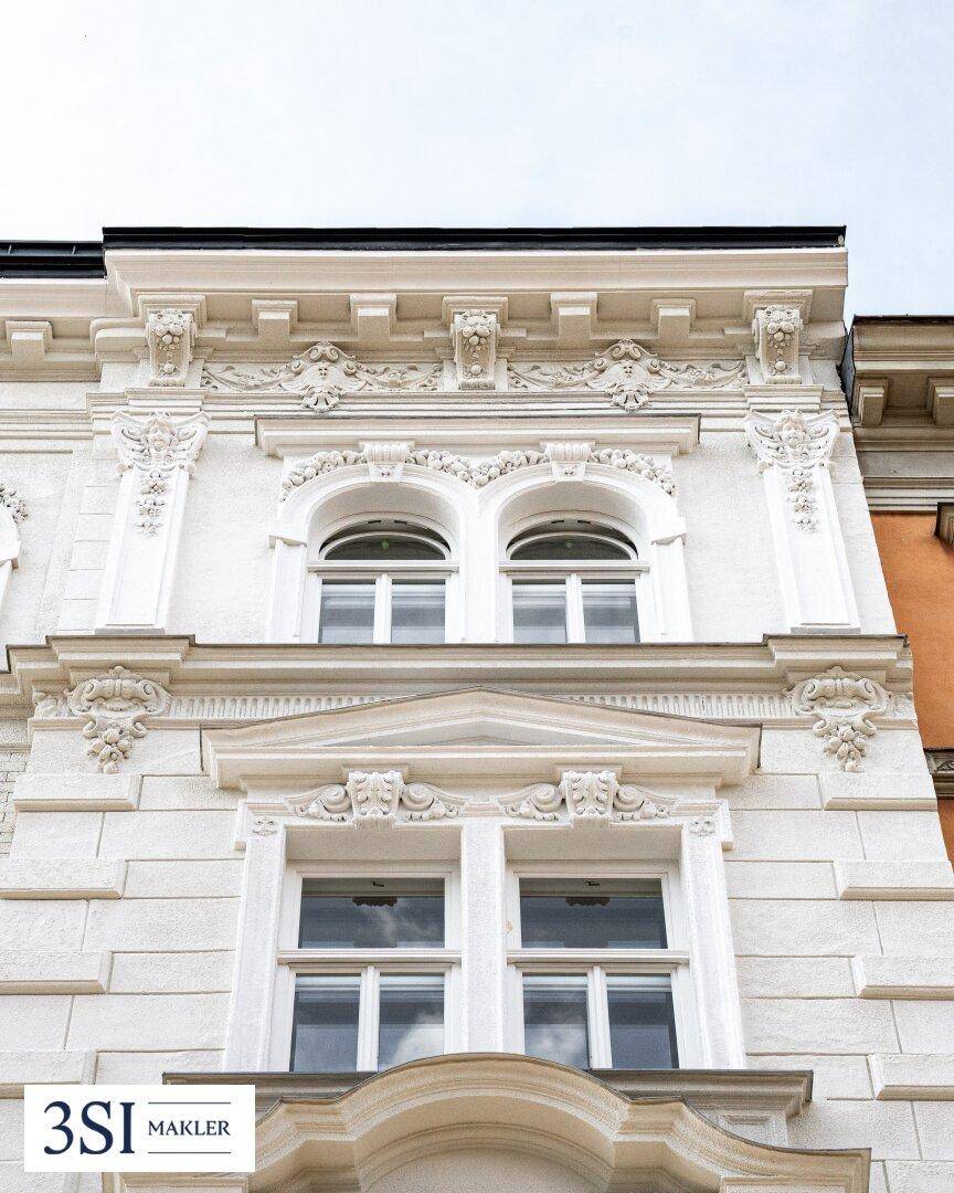 Nahaufnahme der reich verzierten, weißen Fassade mit Rundbogenfenstern und Stuckelementen.