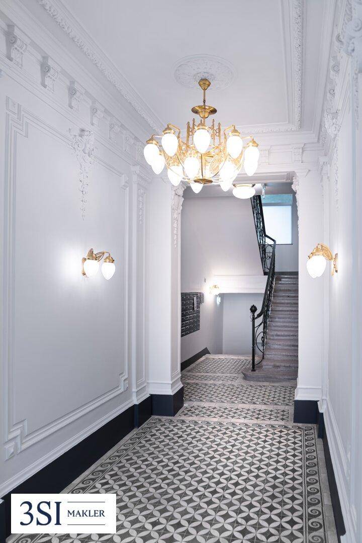 Eleganter Eingangsbereich mit Stuckdecken, Kronleuchter, Wandleuchten und gemustertem Fliesenboden.